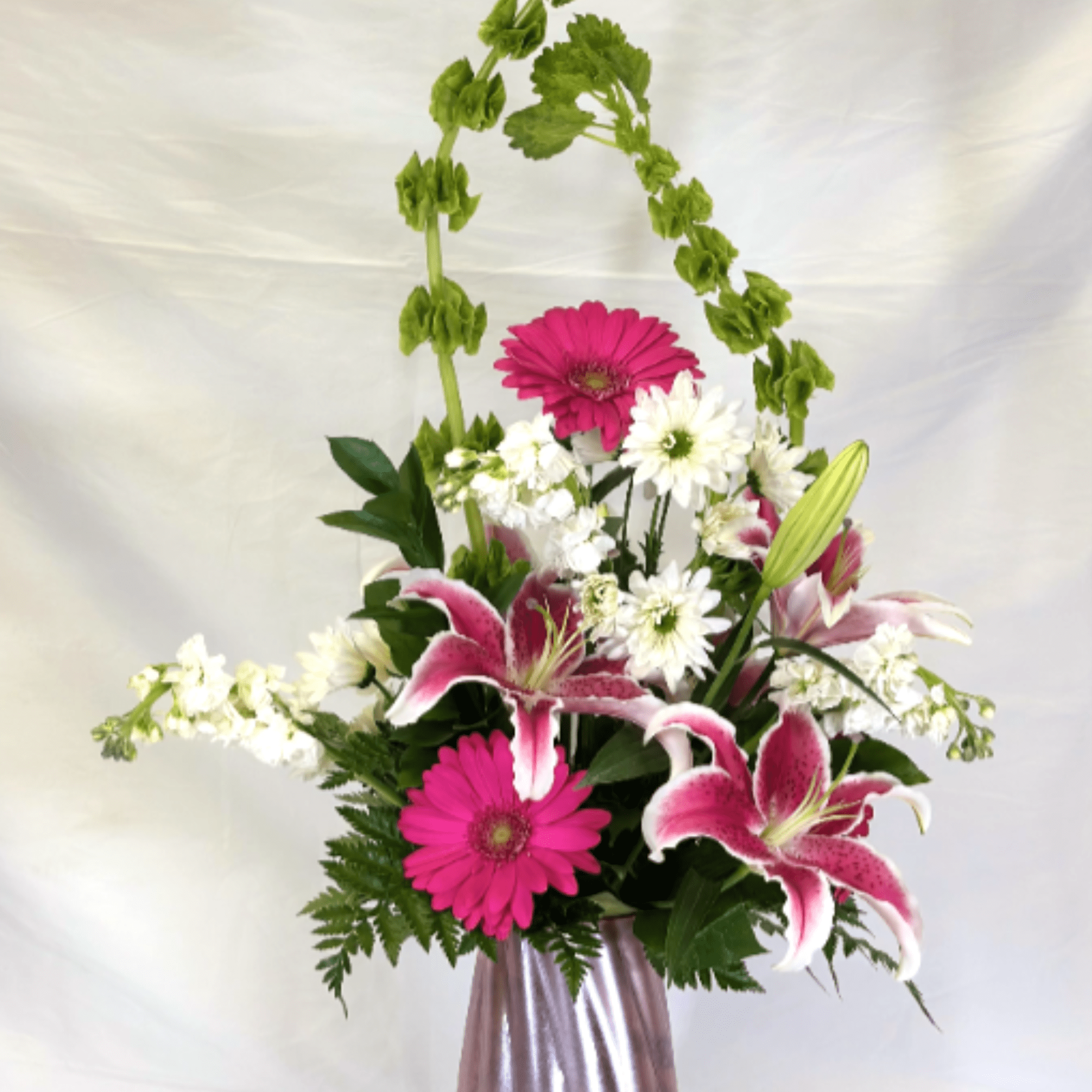 Tall pink and white flower arrangement with green bells of Ireland in a pink metallic vase