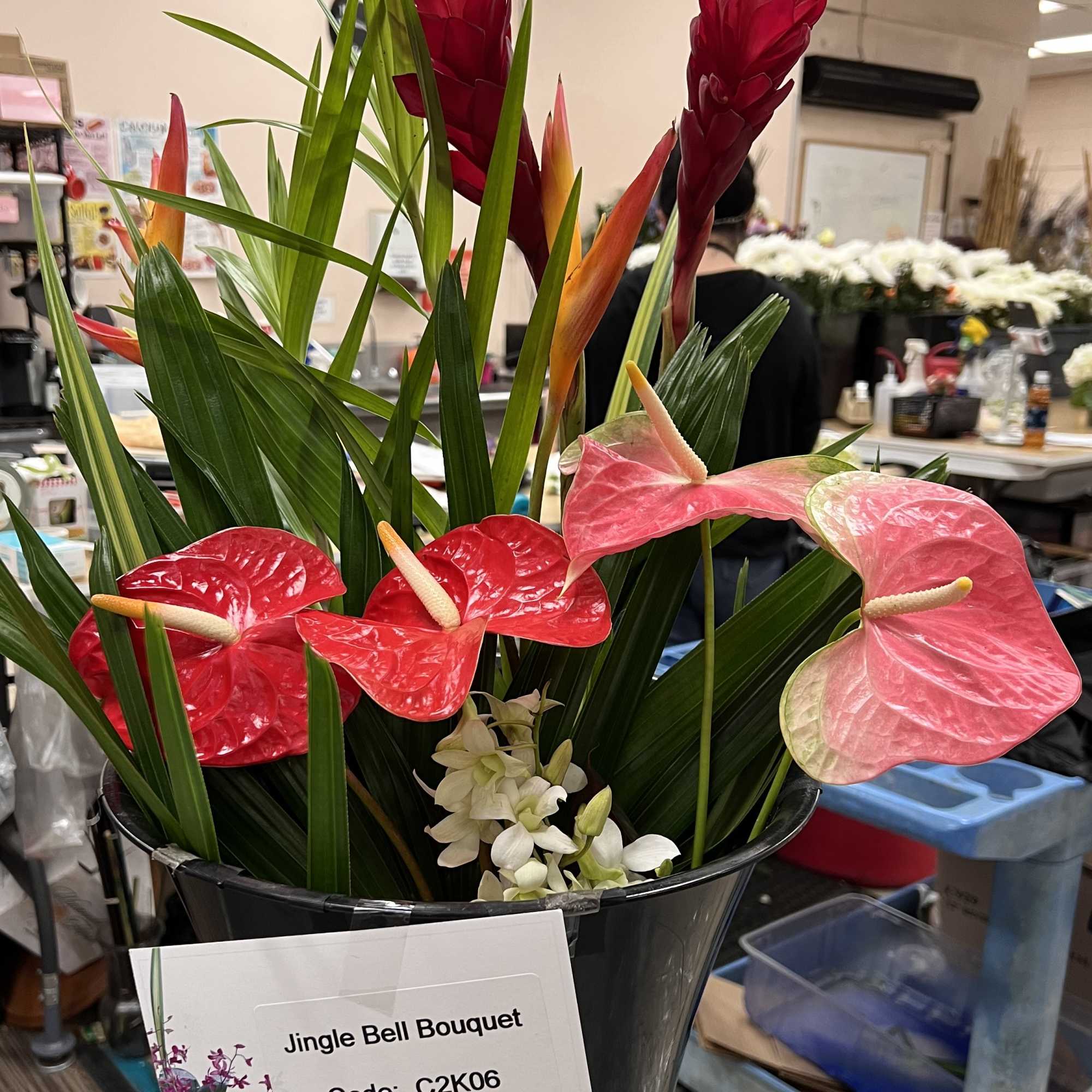 Tall tropical bouquet with red and pink flowers and white orchids in a black bucket