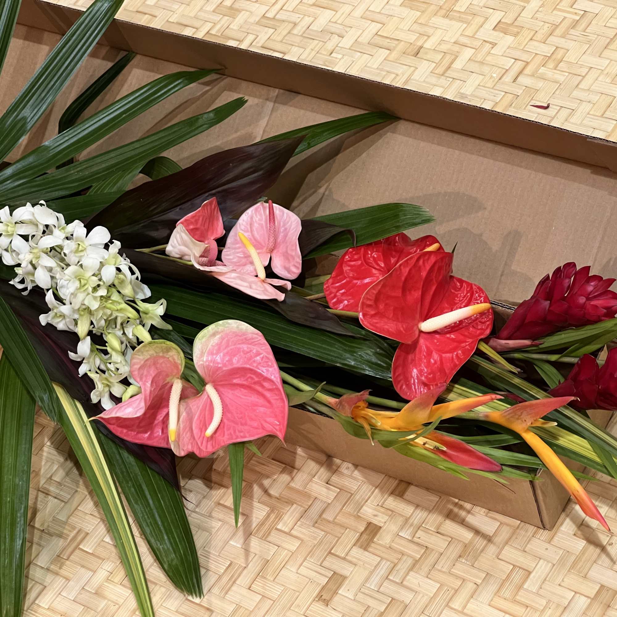 Assorted tropical cut flowers in bright colors arranged loosely in an open cardboard box