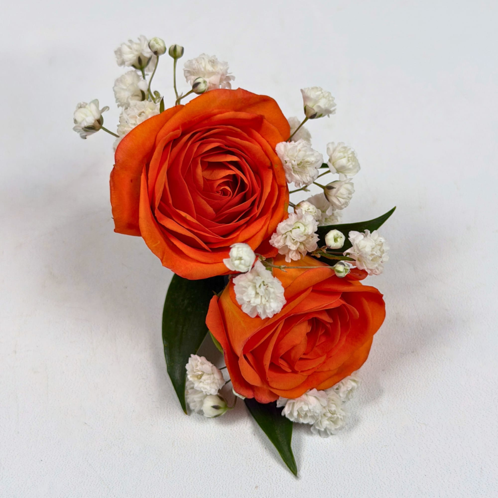 Two vivid orange rose blooms make this boutonniere a bright, celebratory accent
