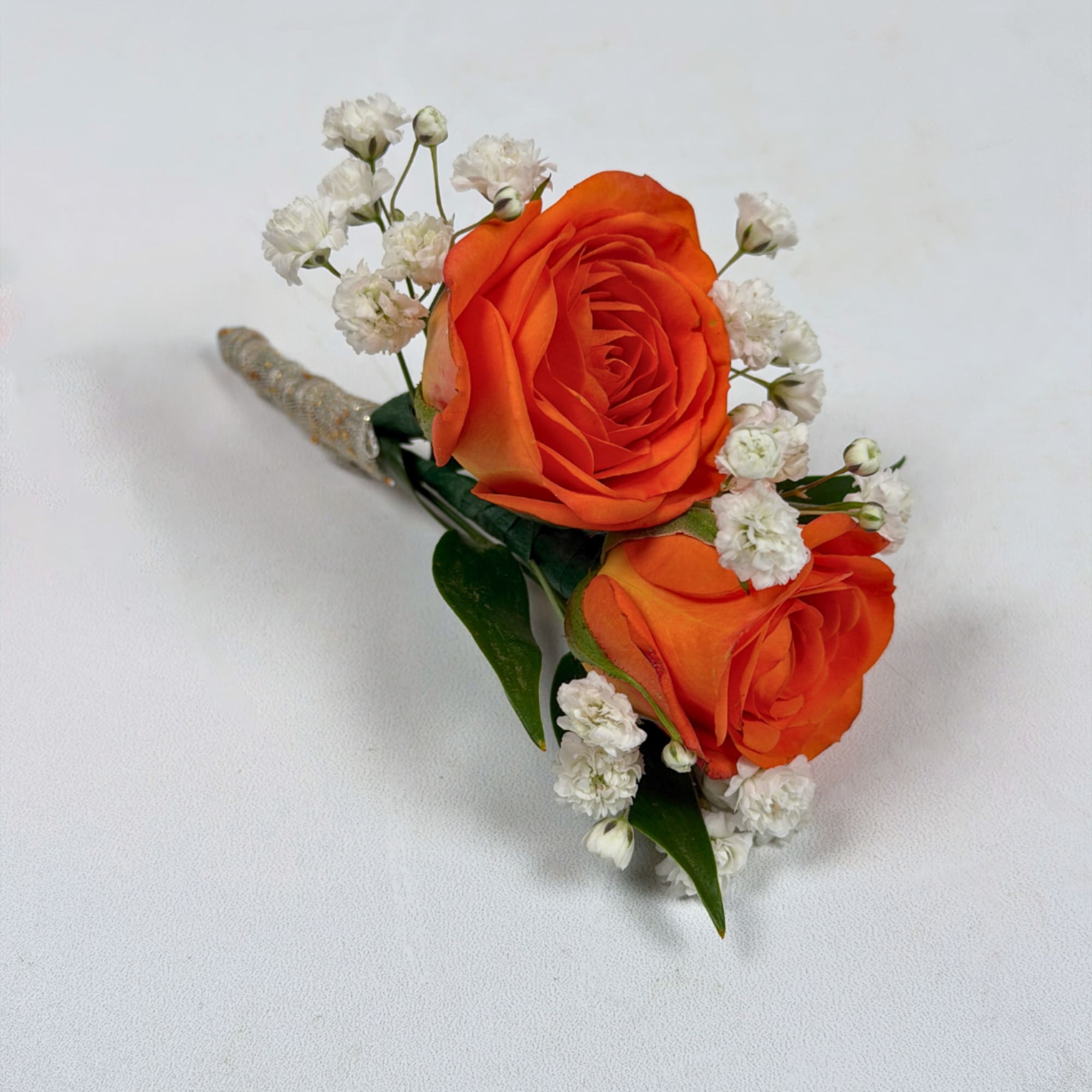 Two vivid orange rose blooms make this boutonniere a bright, celebratory accent