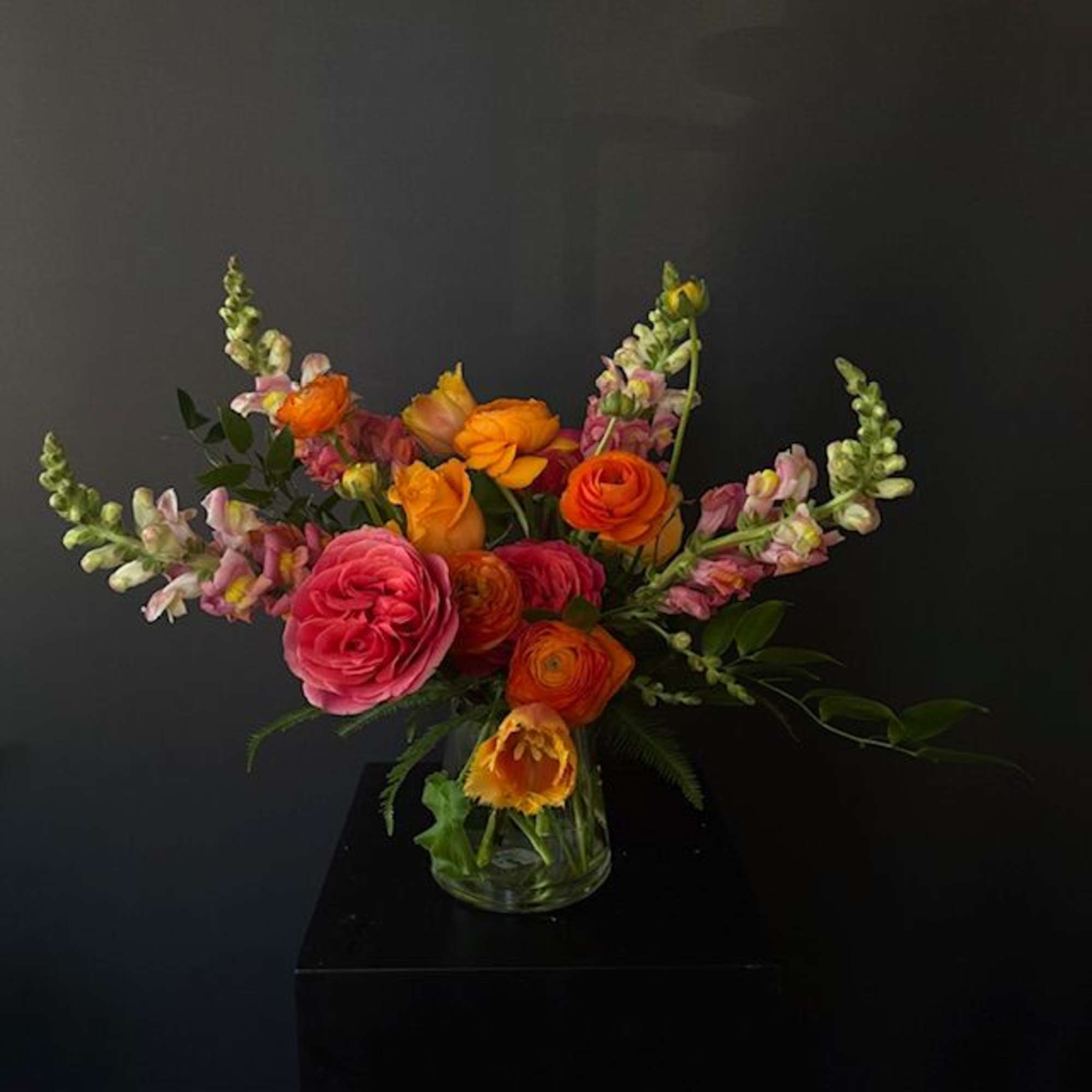 Bright mixed bouquet of orange and pink flowers in a clear glass vase