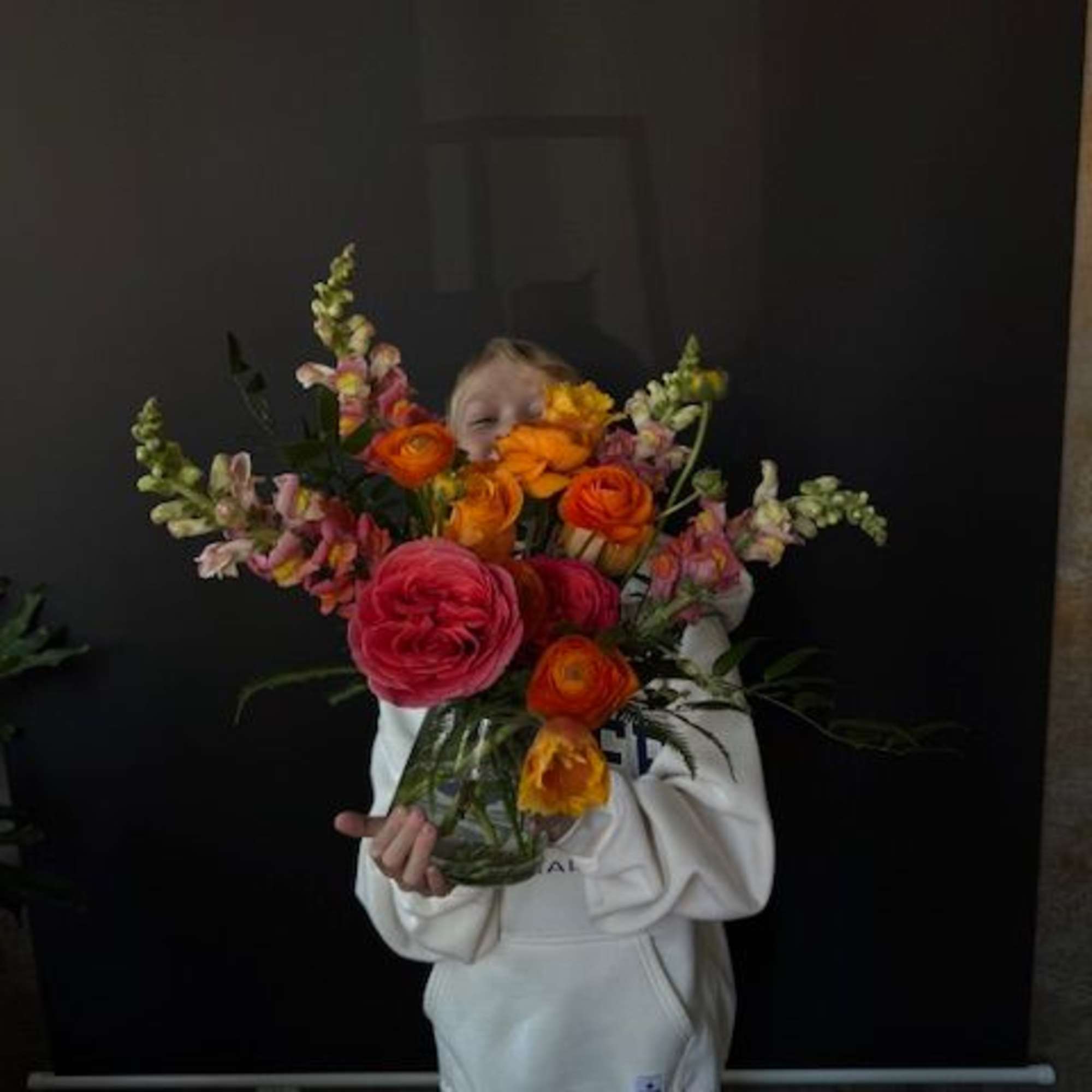 Child holding a large bouquet of orange, pink, and yellow flowers