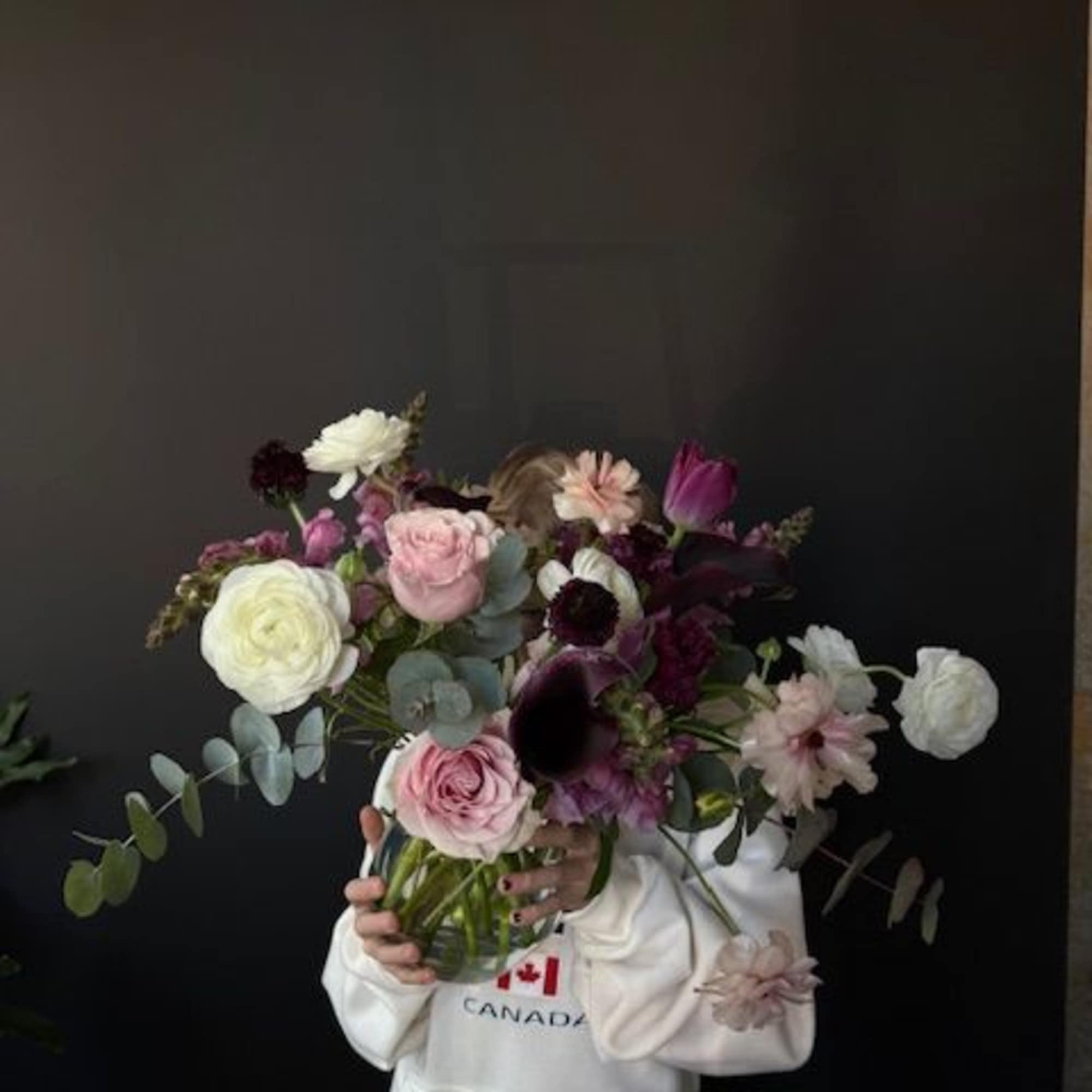 Handheld bouquet of pink, white, and dark purple flowers in a glass vase