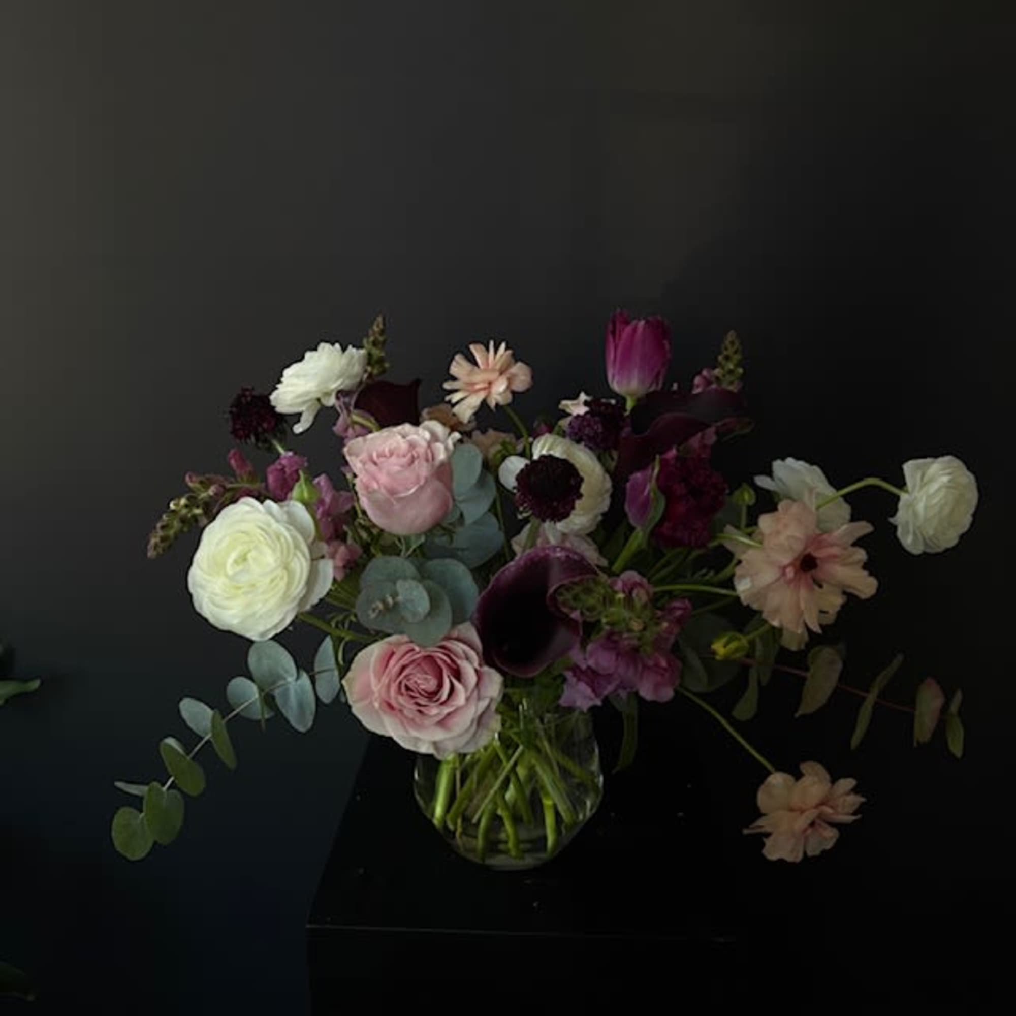 Mixed bouquet of pink, white, and dark purple flowers in a glass vase