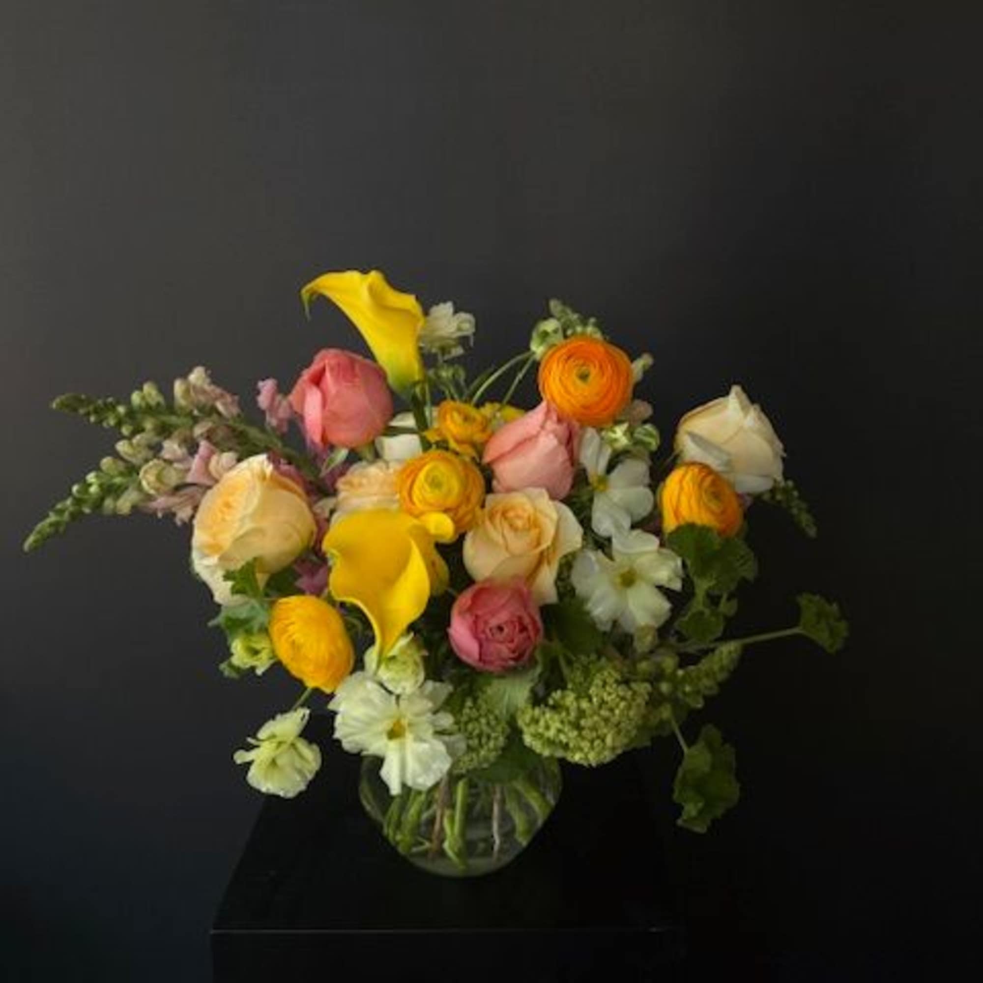 Mixed bouquet of roses, calla lilies, and ranunculus in a glass vase