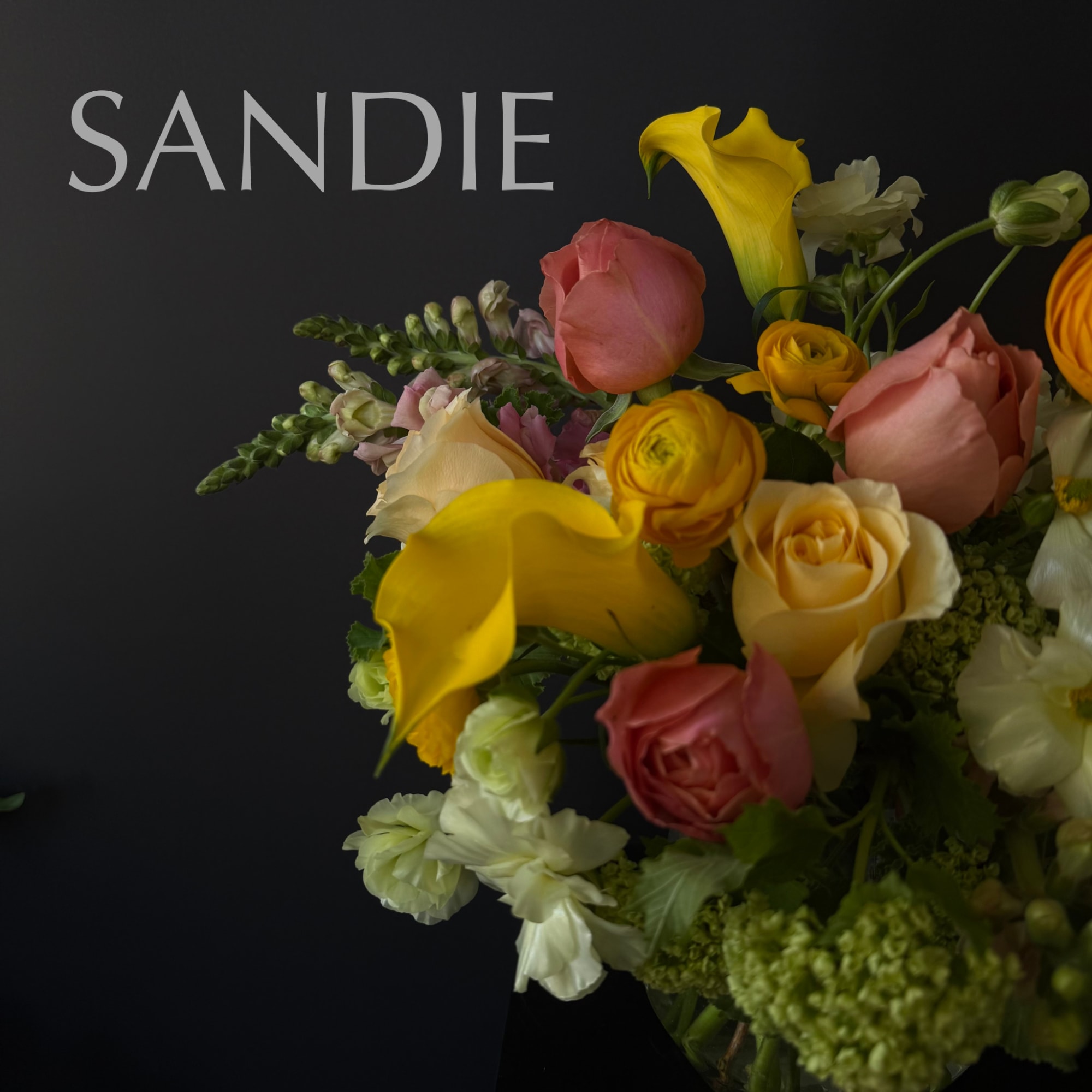 Bouquet of yellow calla lilies, roses, and white flowers against a dark background
