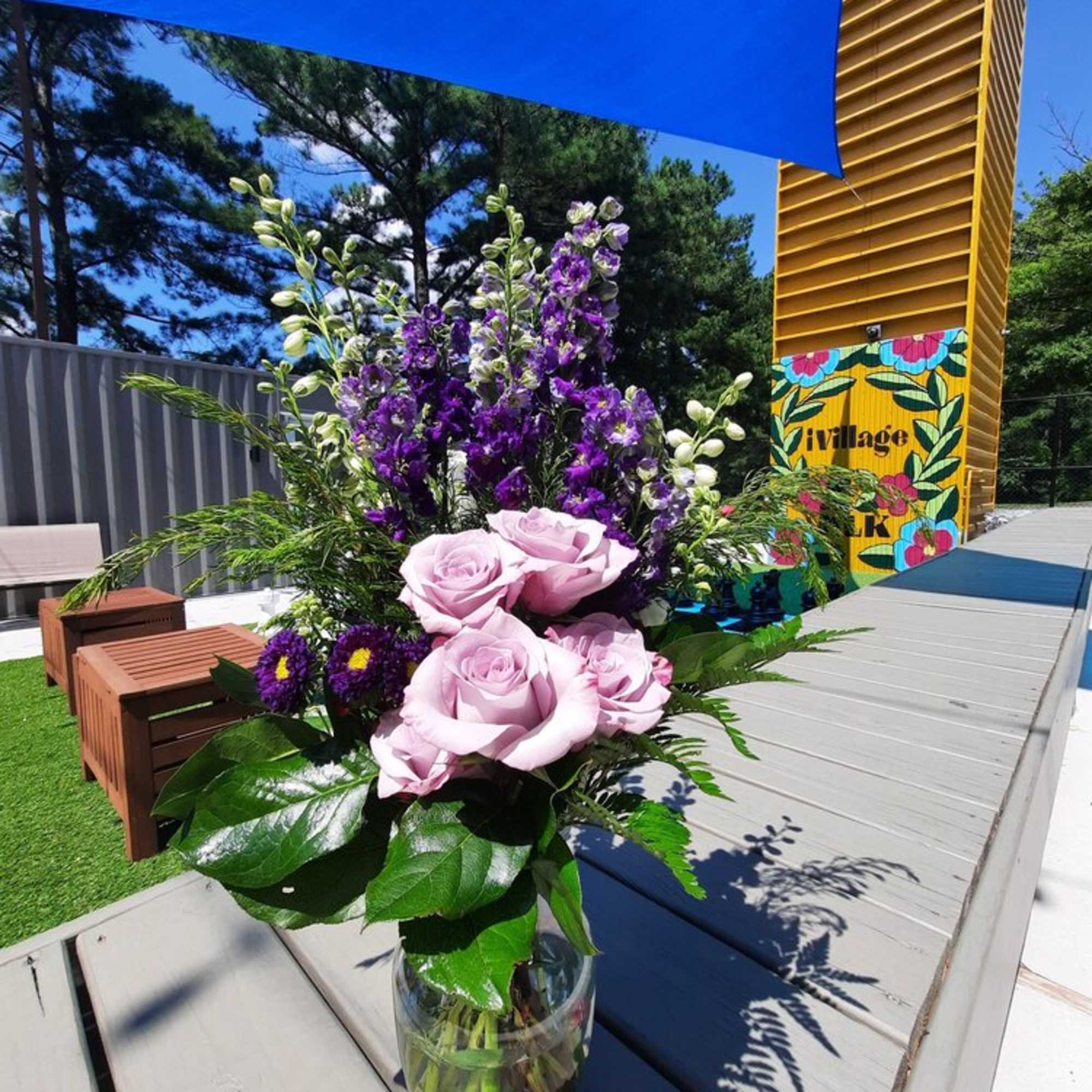 Pink roses and purple flowers in a glass vase outdoors