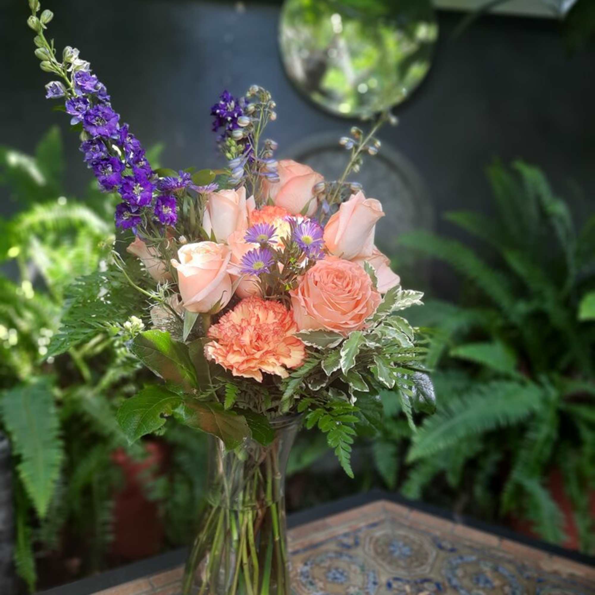 Peach roses and purple flowers arranged in a clear glass vase