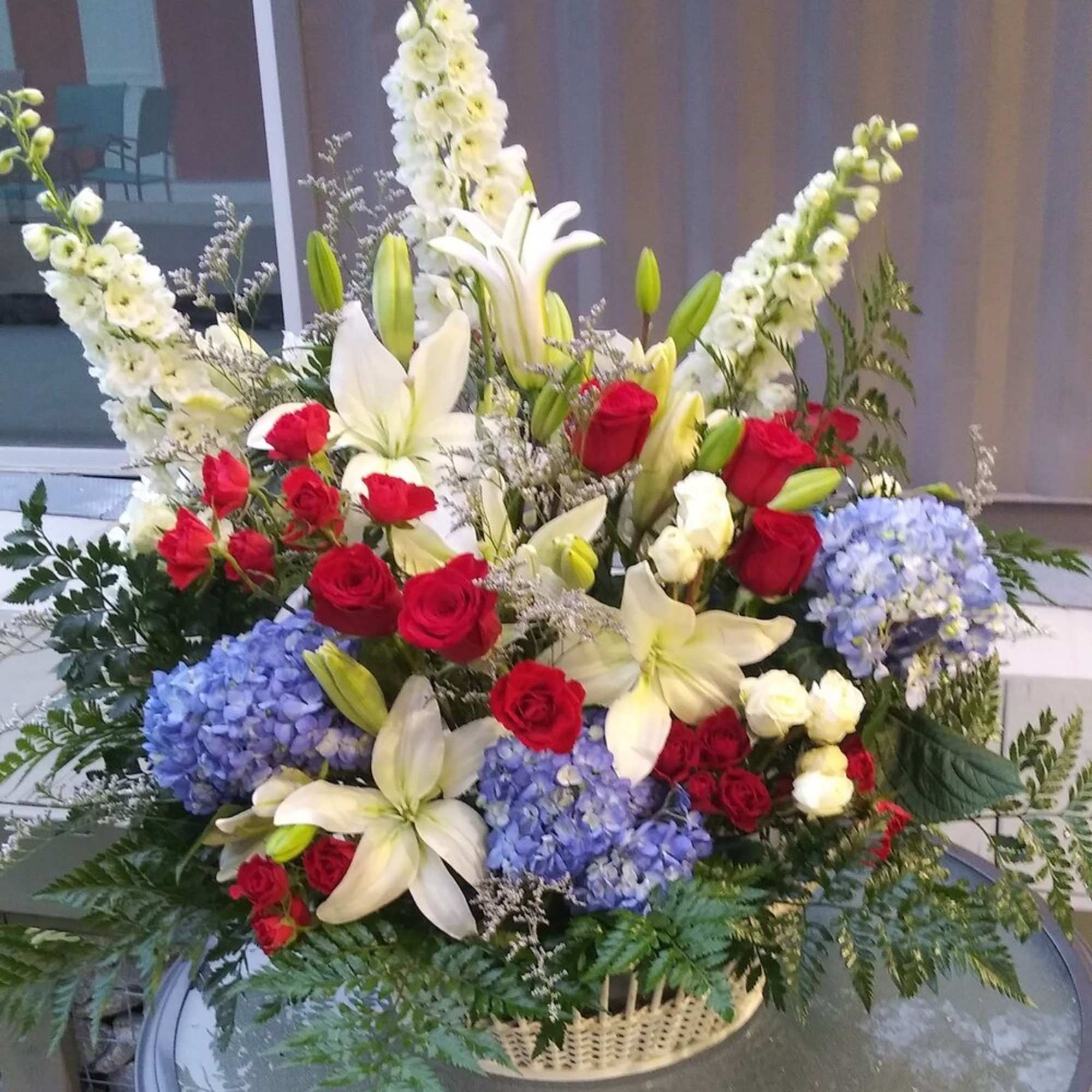 Large floral arrangement with red roses, white lilies, and blue hydrangeas in a basket