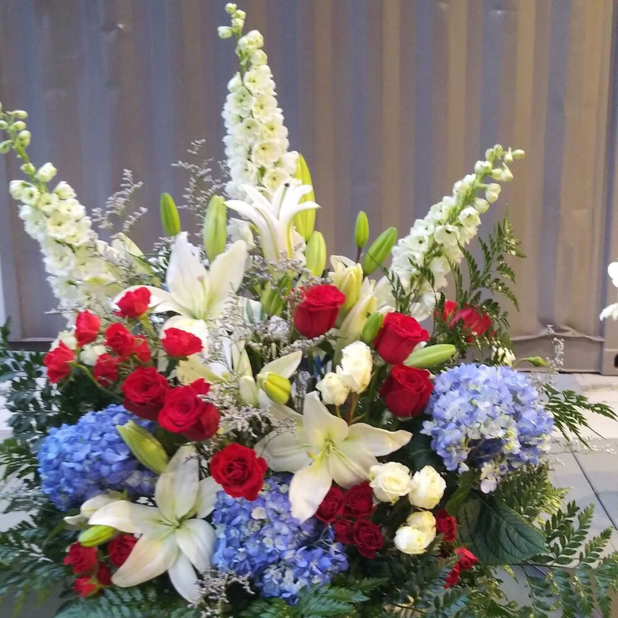 Large basket arrangement with red roses, white lilies, and blue hydrangeas