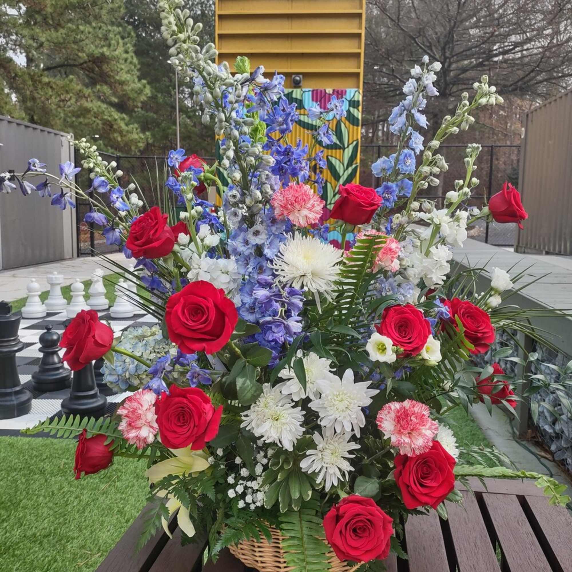 Basket arrangement with red roses, blue delphinium, and white daisies