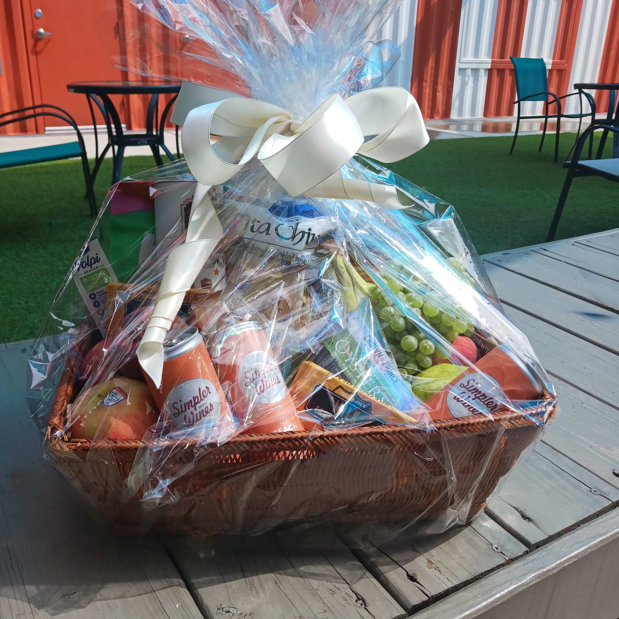 Gift basket with snacks and drinks wrapped in clear cellophane and a white bow
