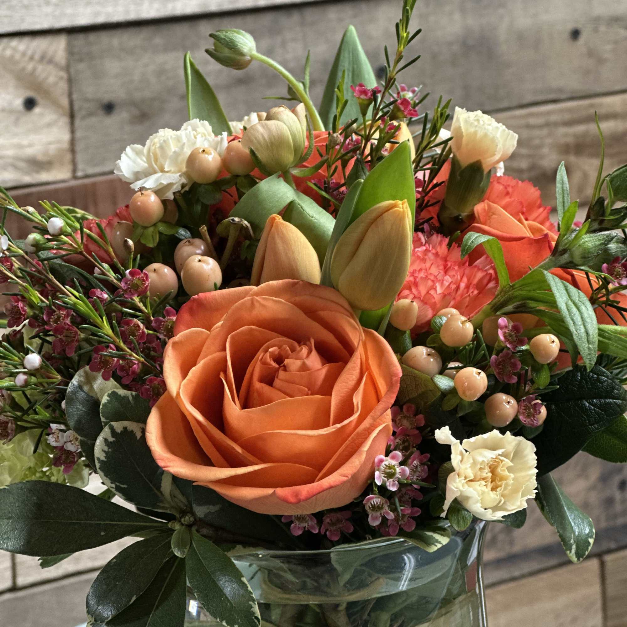 A vibrant orange rose takes center stage in this rounded flower arrangement