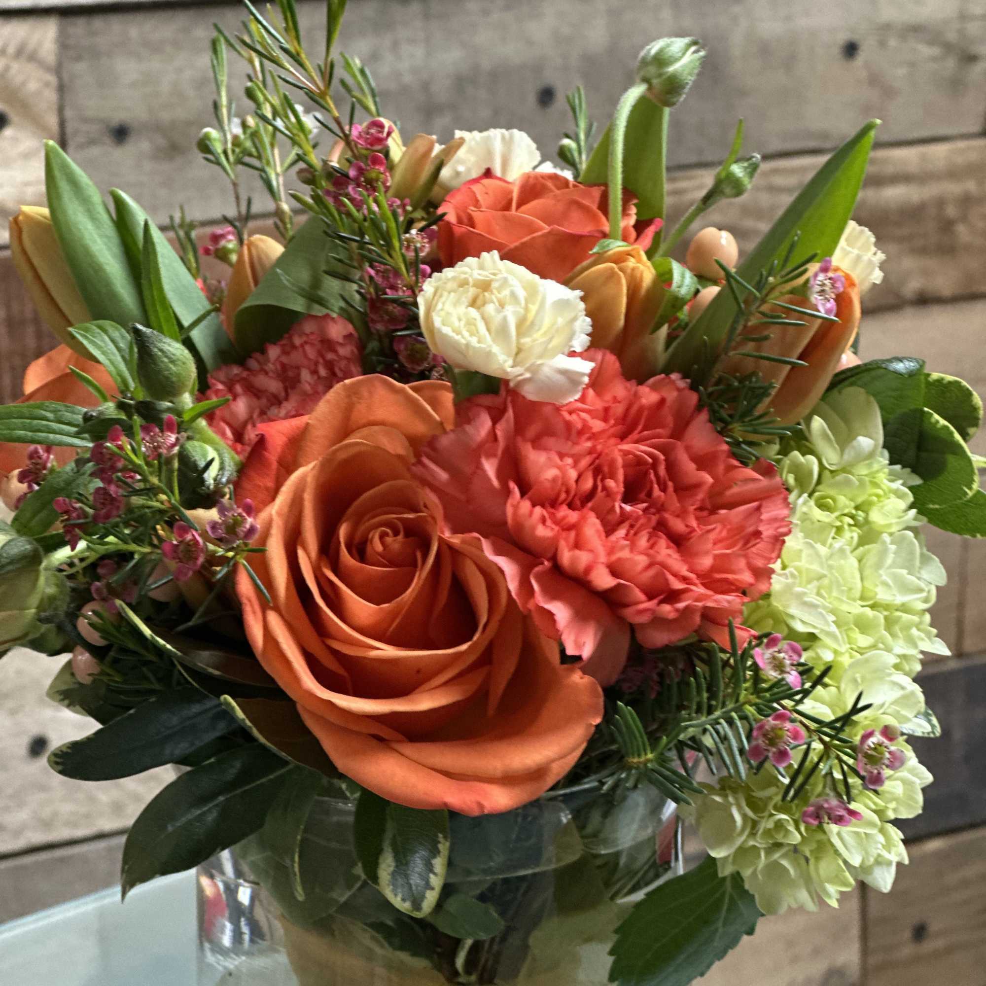 A vibrant orange rose takes center stage in this rounded flower arrangement
