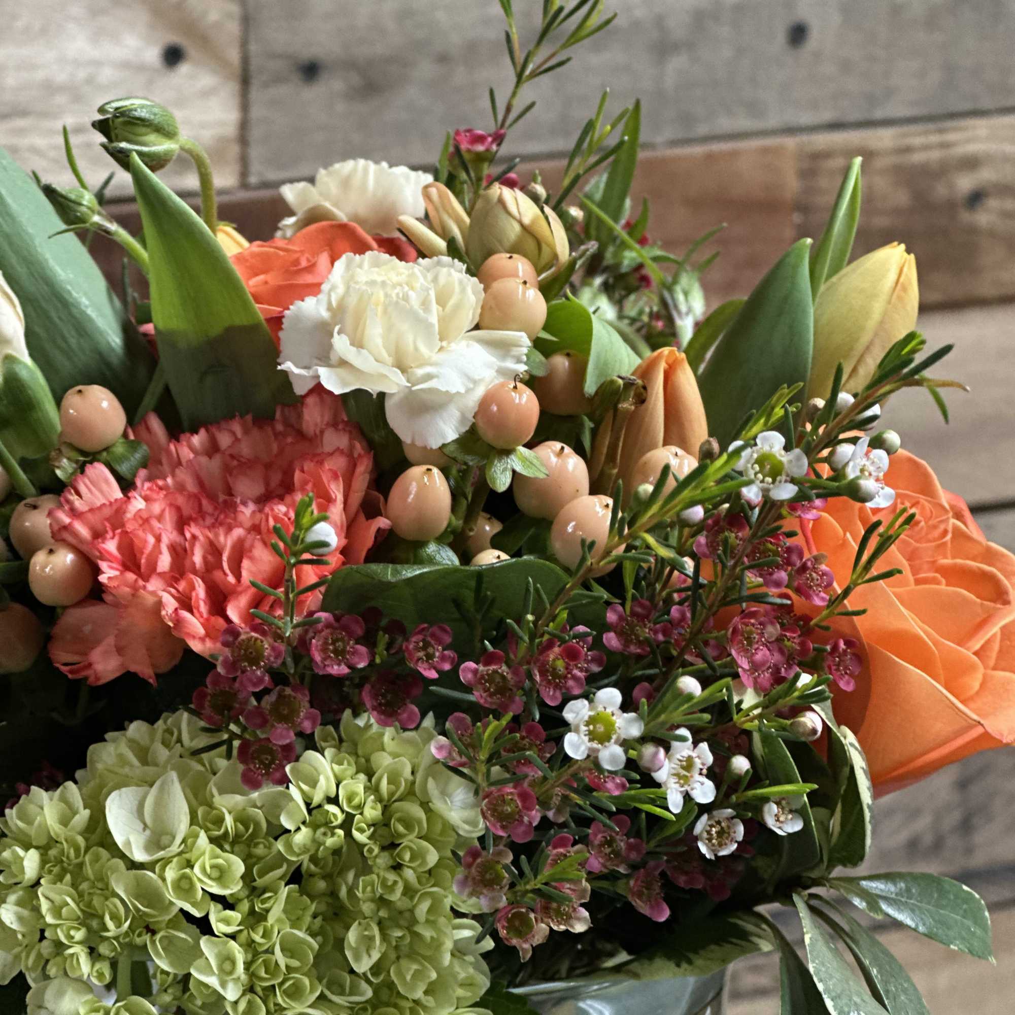A vibrant orange rose takes center stage in this rounded flower arrangement