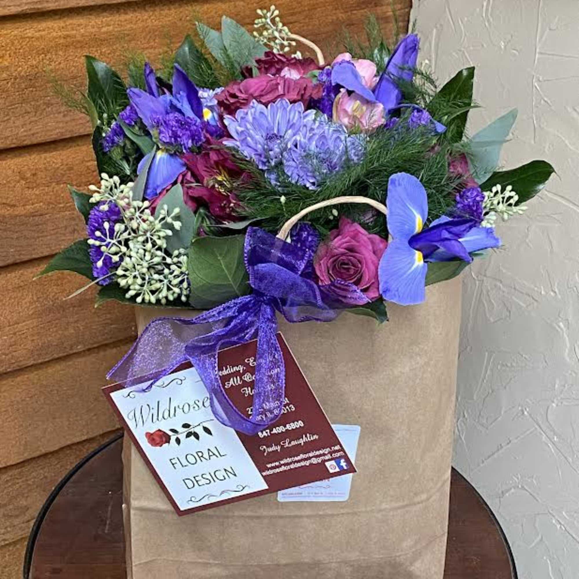 Purple and pink flower arrangement in a brown paper bag with a ribbon