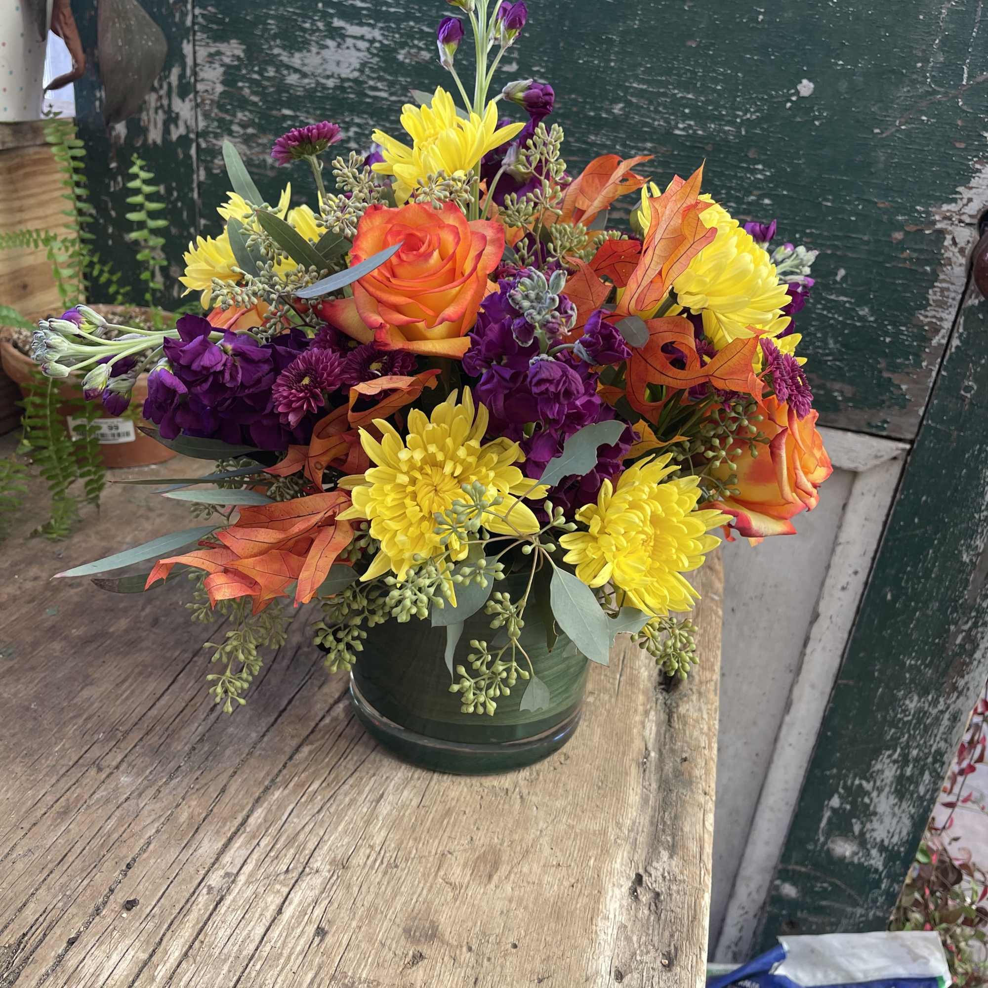 Colorful bouquet in a dark green vase with orange roses and yellow and purple blooms