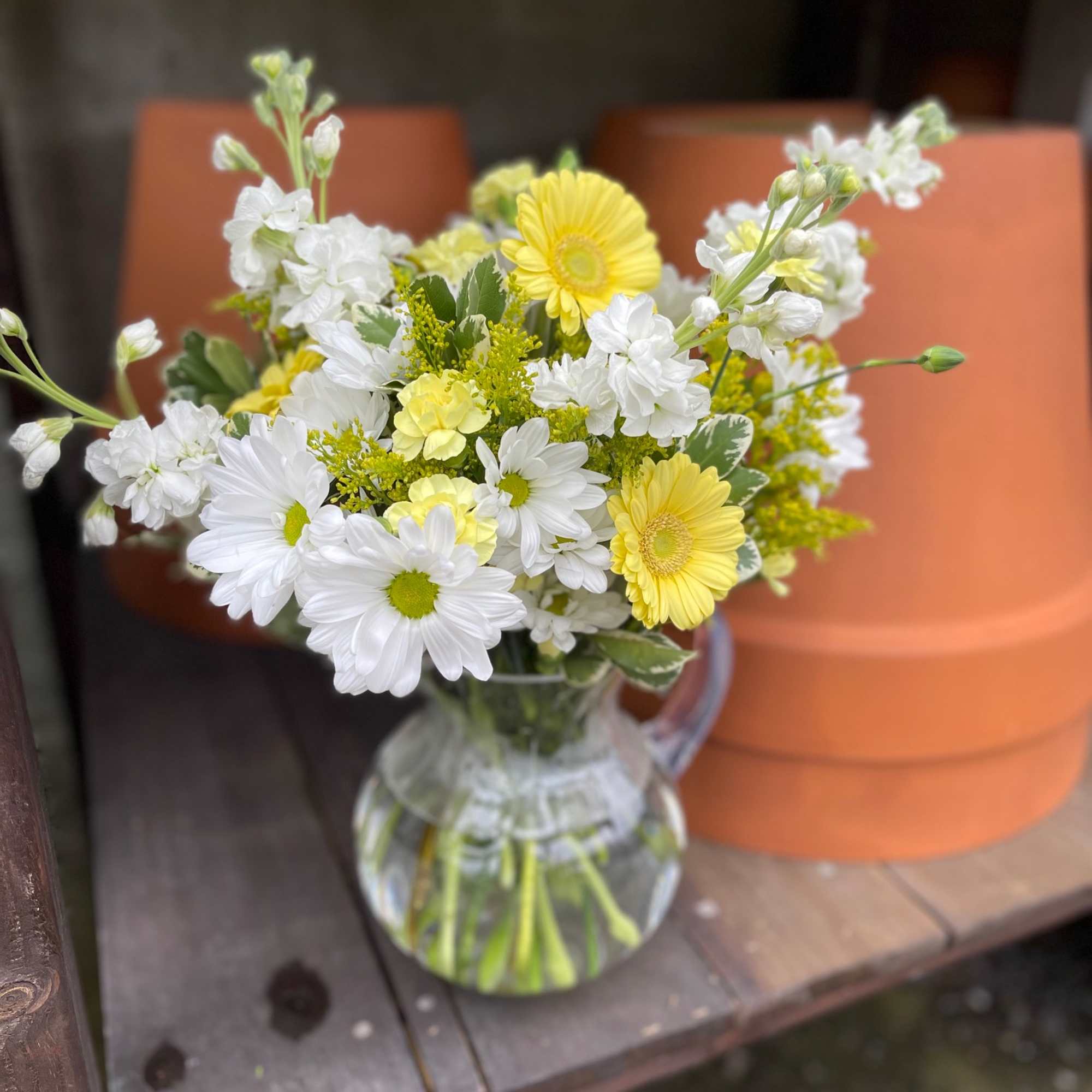 White and yellow daisy bouquet in a clear glass pitcher
