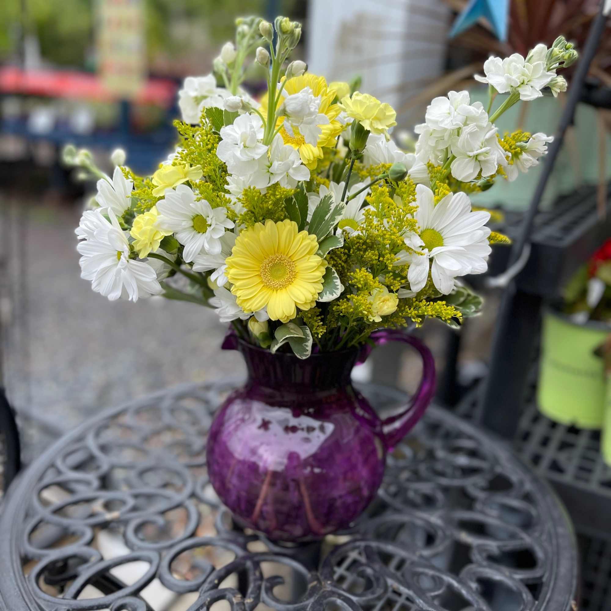 Yellow and white flowers arranged in a purple glass pitcher