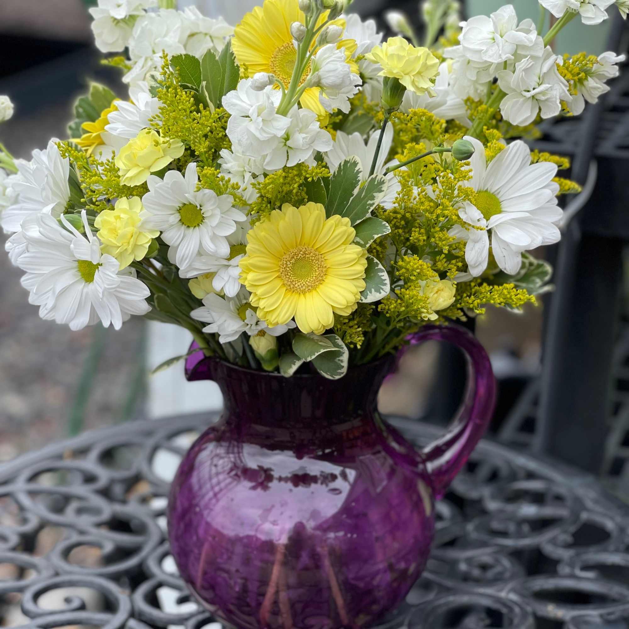 Yellow and white mixed flowers in a purple glass pitcher vase