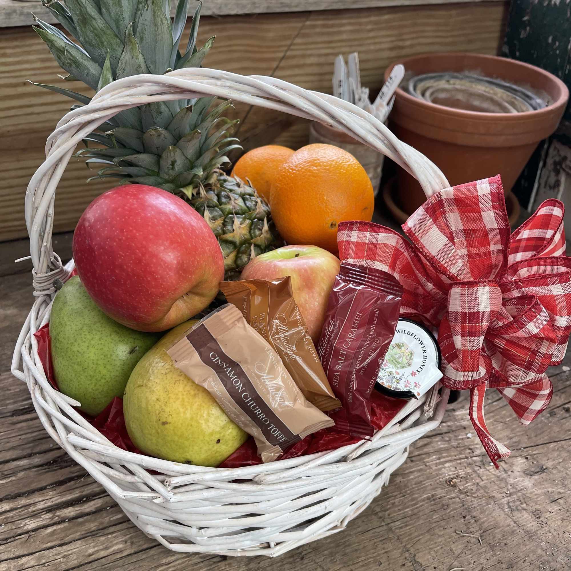 Fruit basket with pineapple, apples, pears, oranges, and wrapped candies