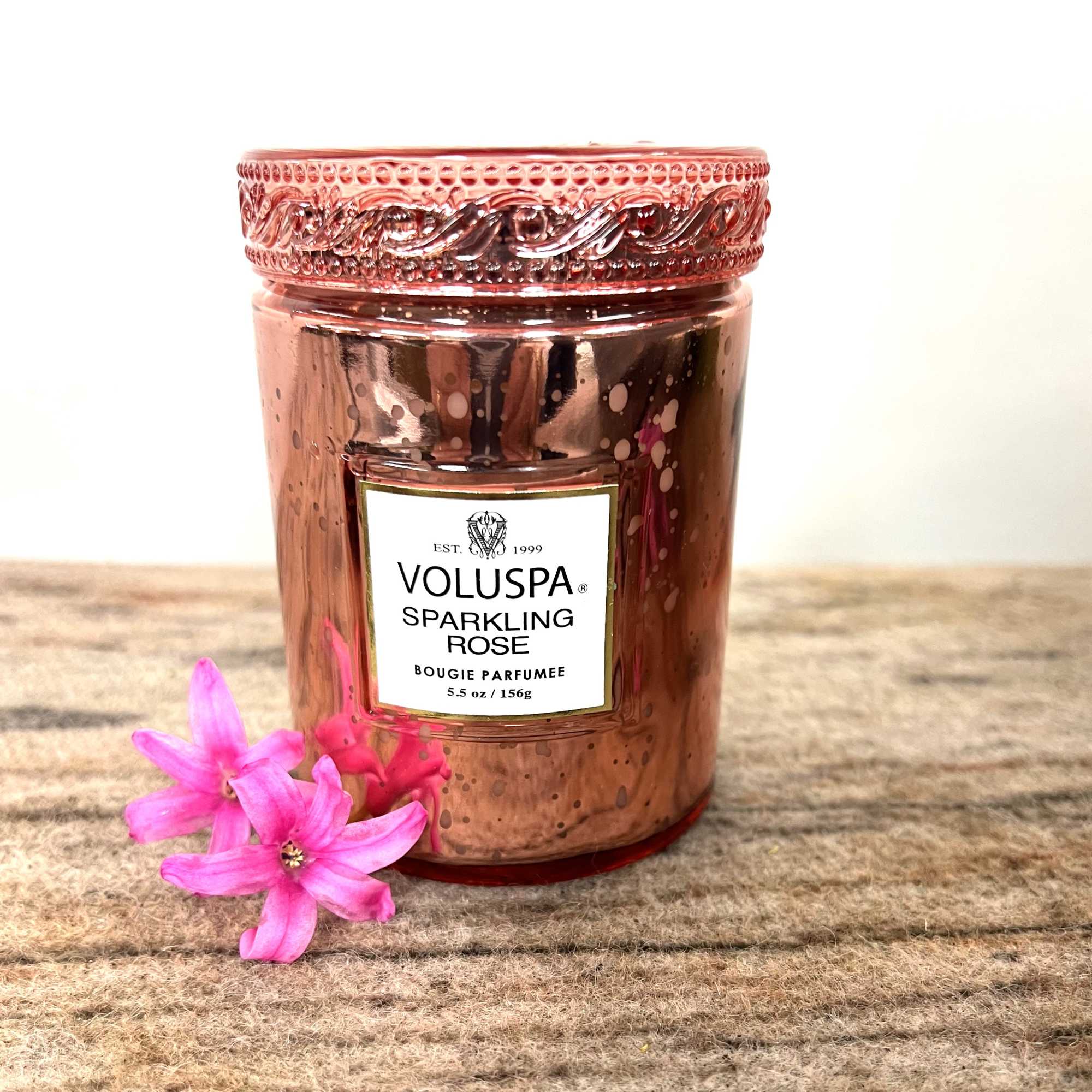 Rose-colored candle jar with pink flowers beside it