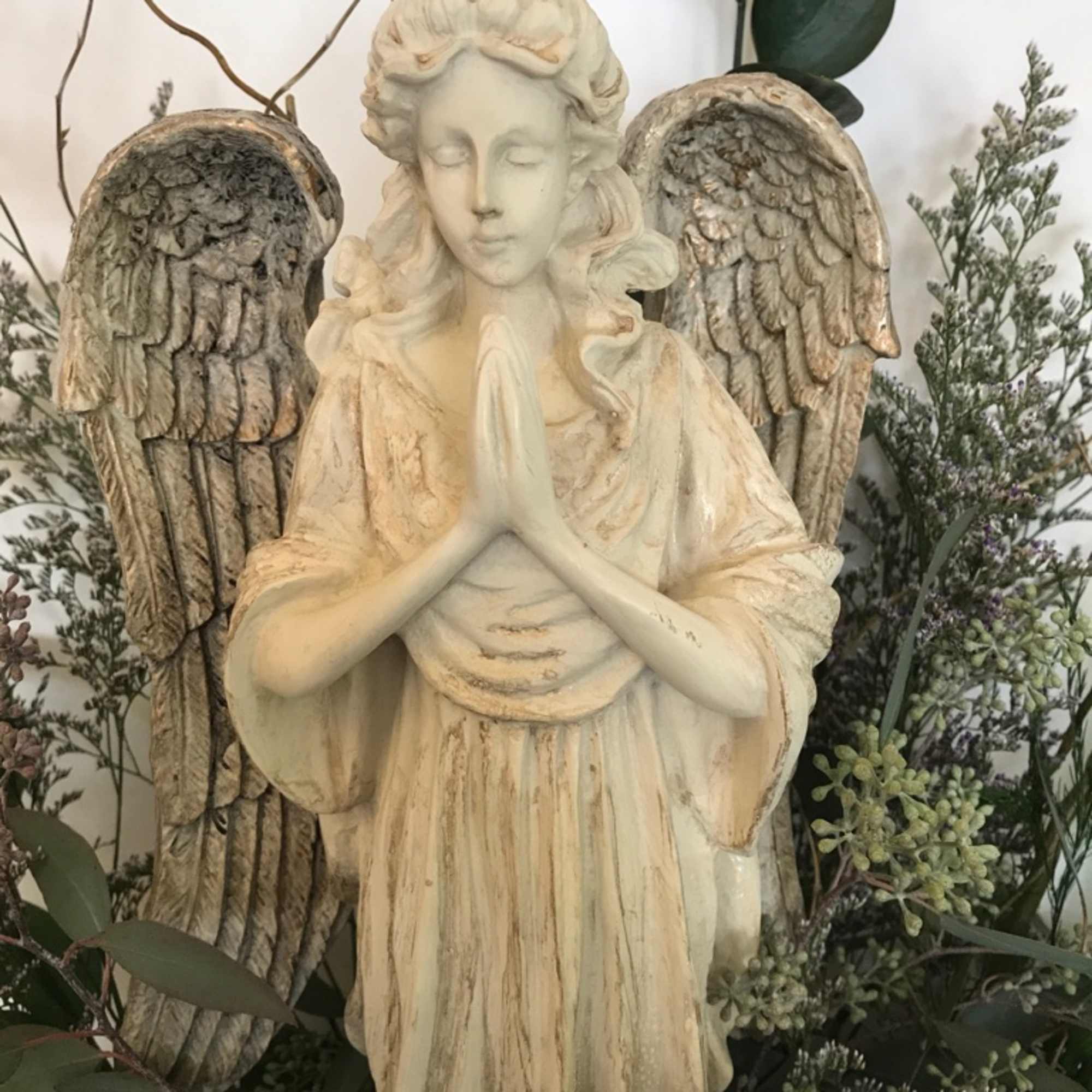 Angel statue with wings surrounded by greenery and small flowers