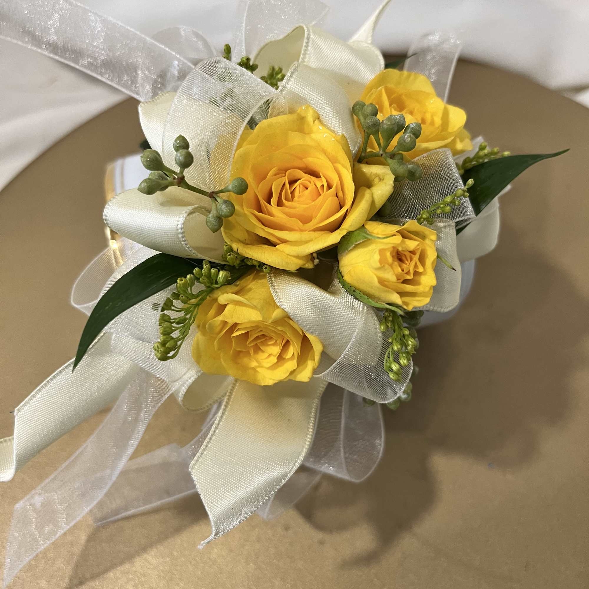 Small bouquet of yellow roses with white ribbon and greenery