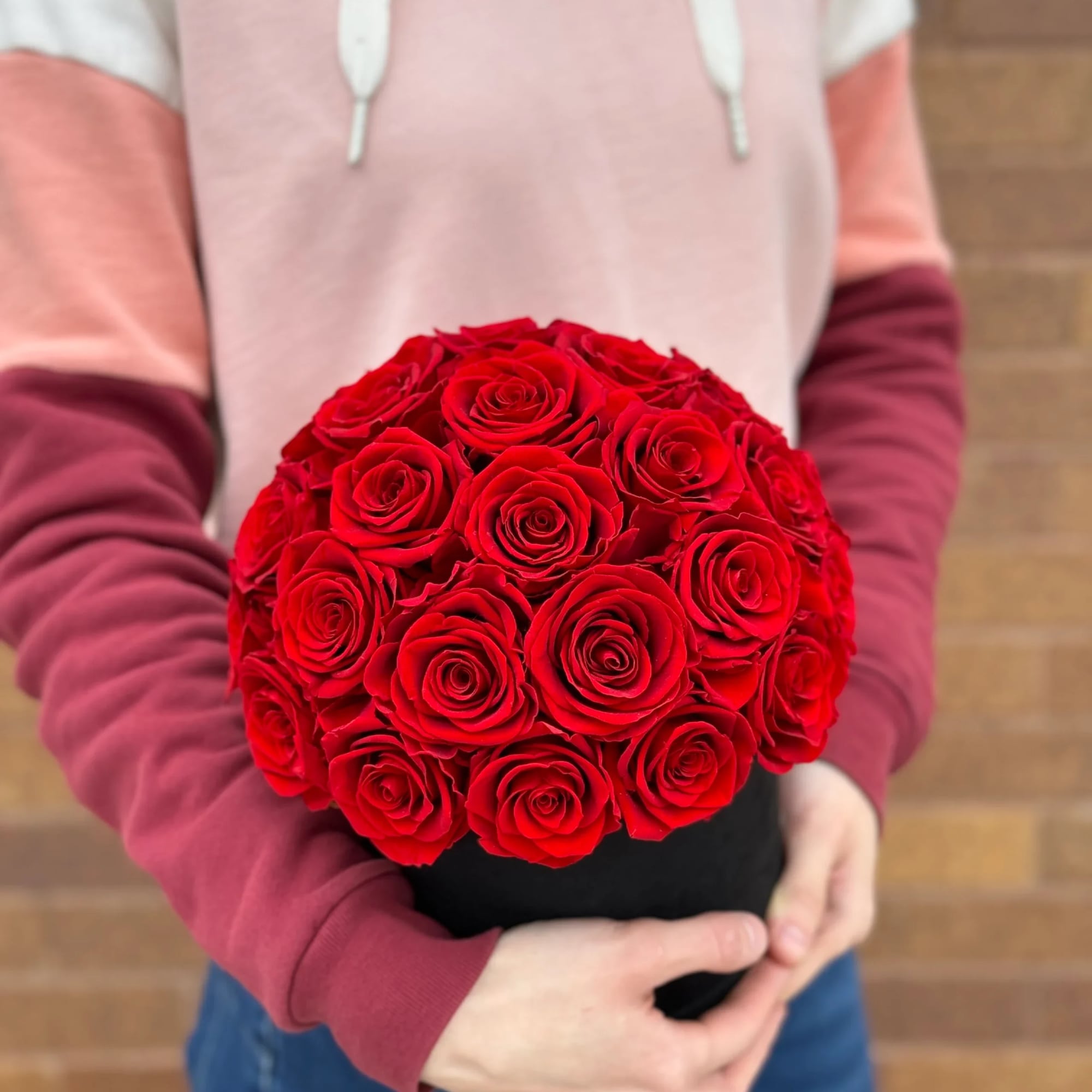 Round bouquet of red roses held in both hands