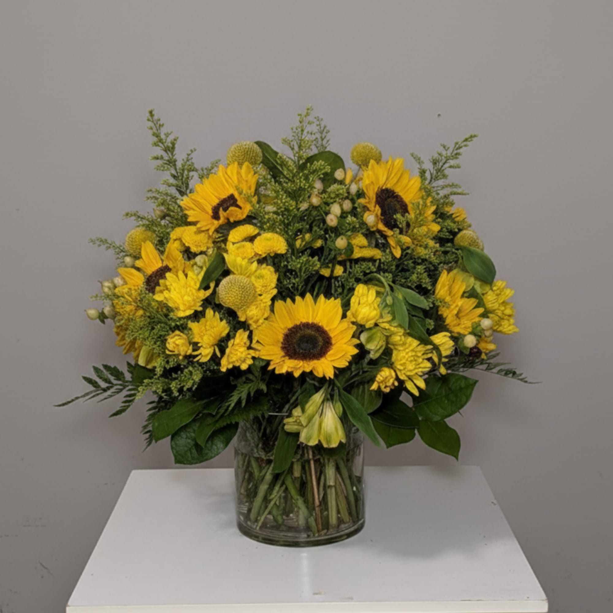Yellow sunflower and chrysanthemum arrangement in a clear glass vase