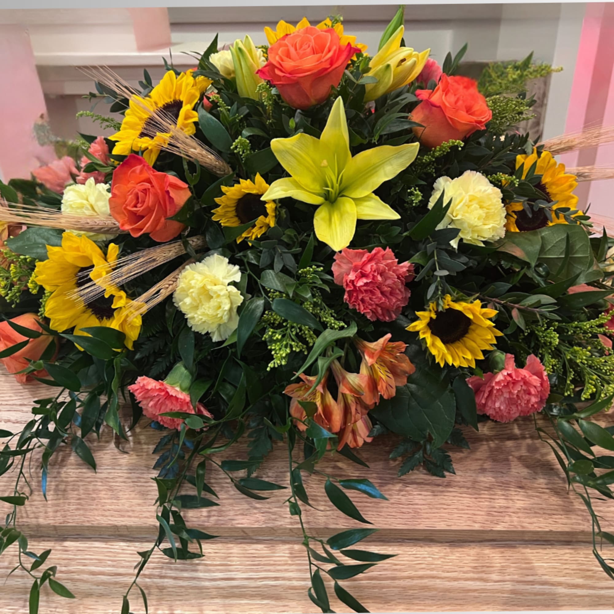 This Bright Casket Spray contains sunflowers, lilies, orange roses, and orange and