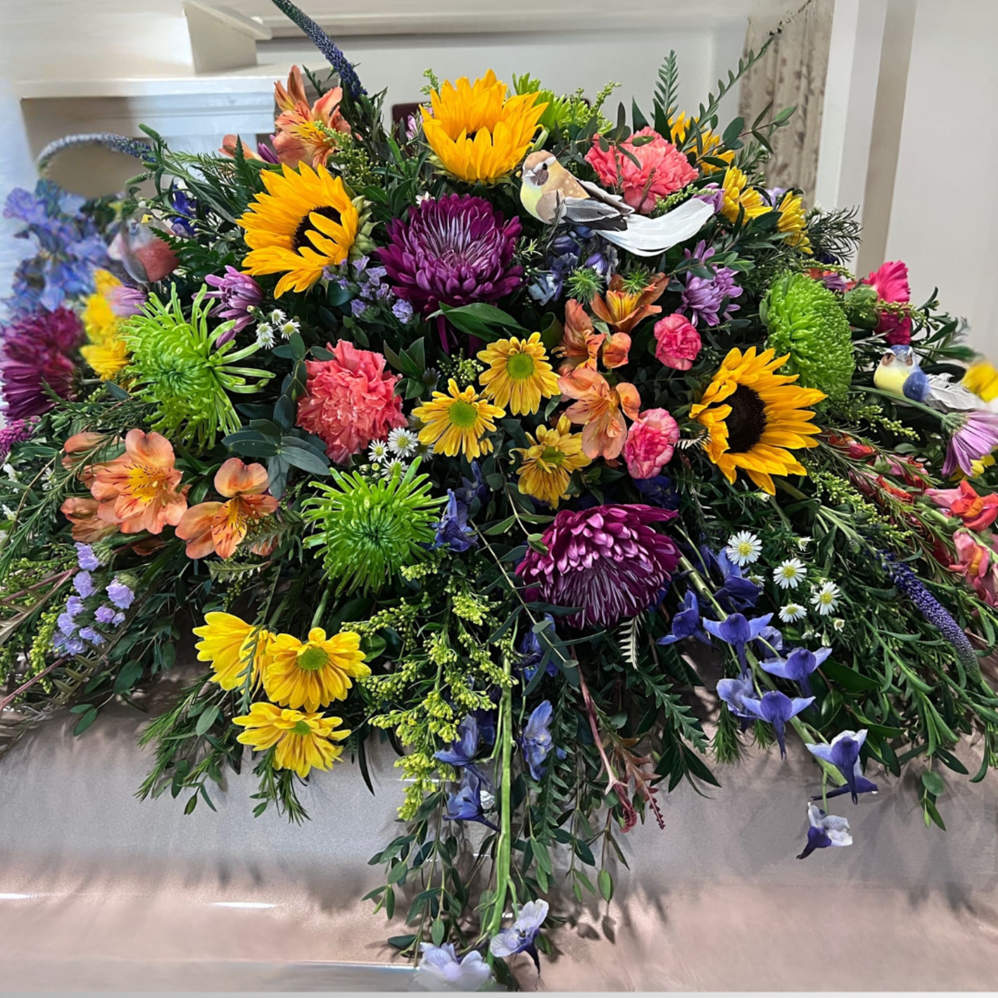 This colorful casket spray includes a variety of wildflowers