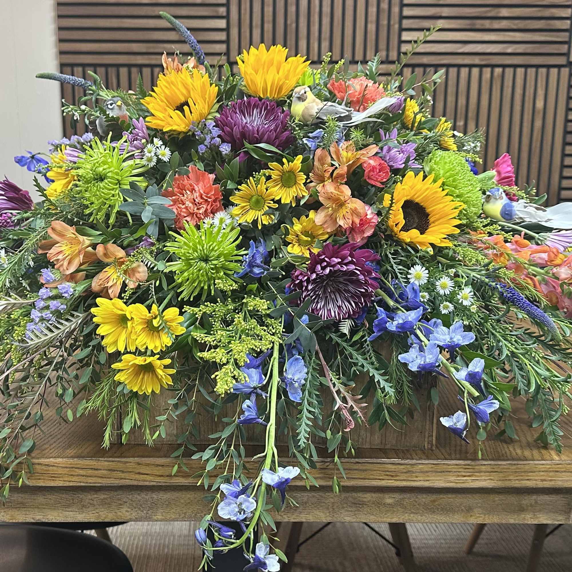 This colorful casket spray includes a variety of wildflowers