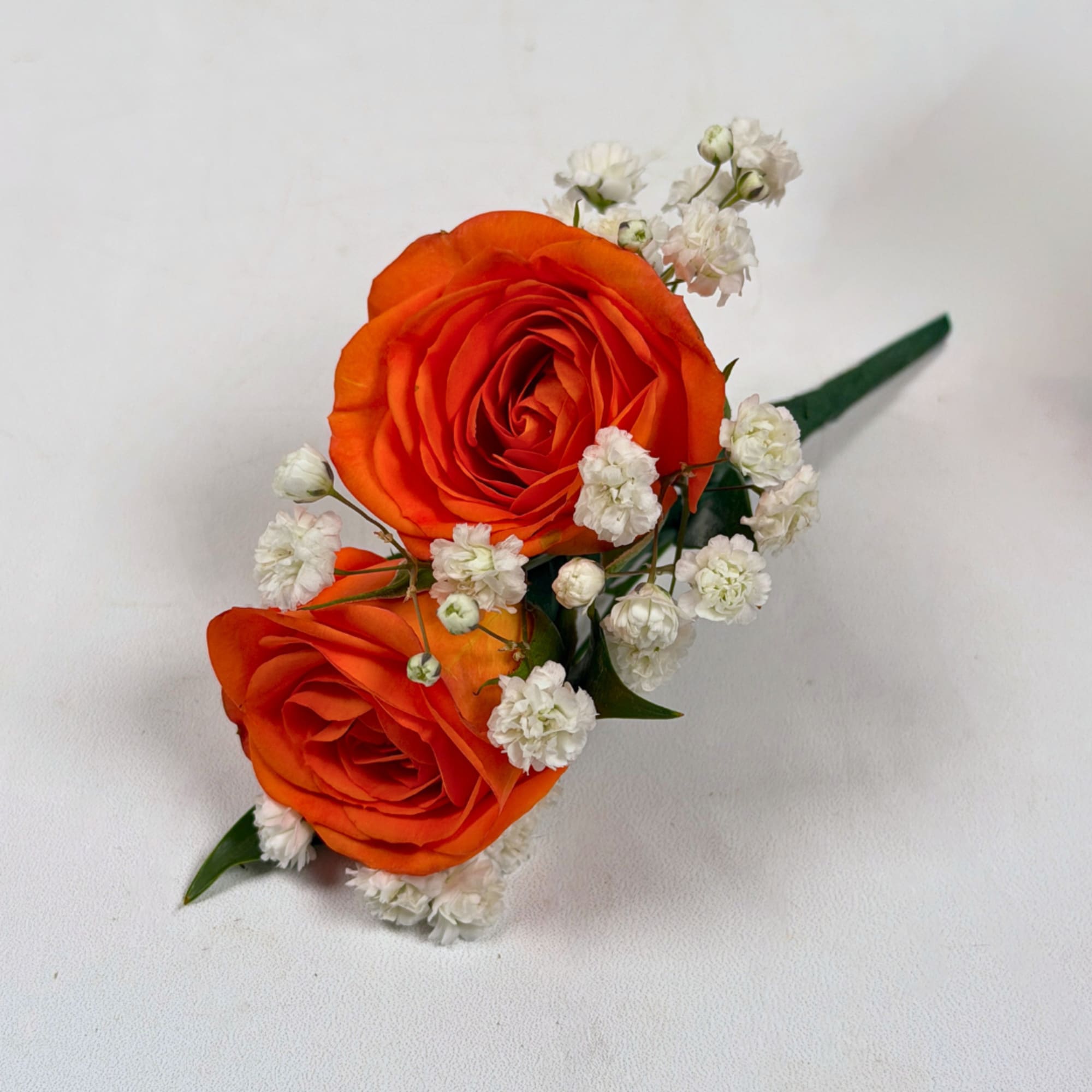 Two vivid orange rose blooms make this boutonniere a bright, celebratory accent