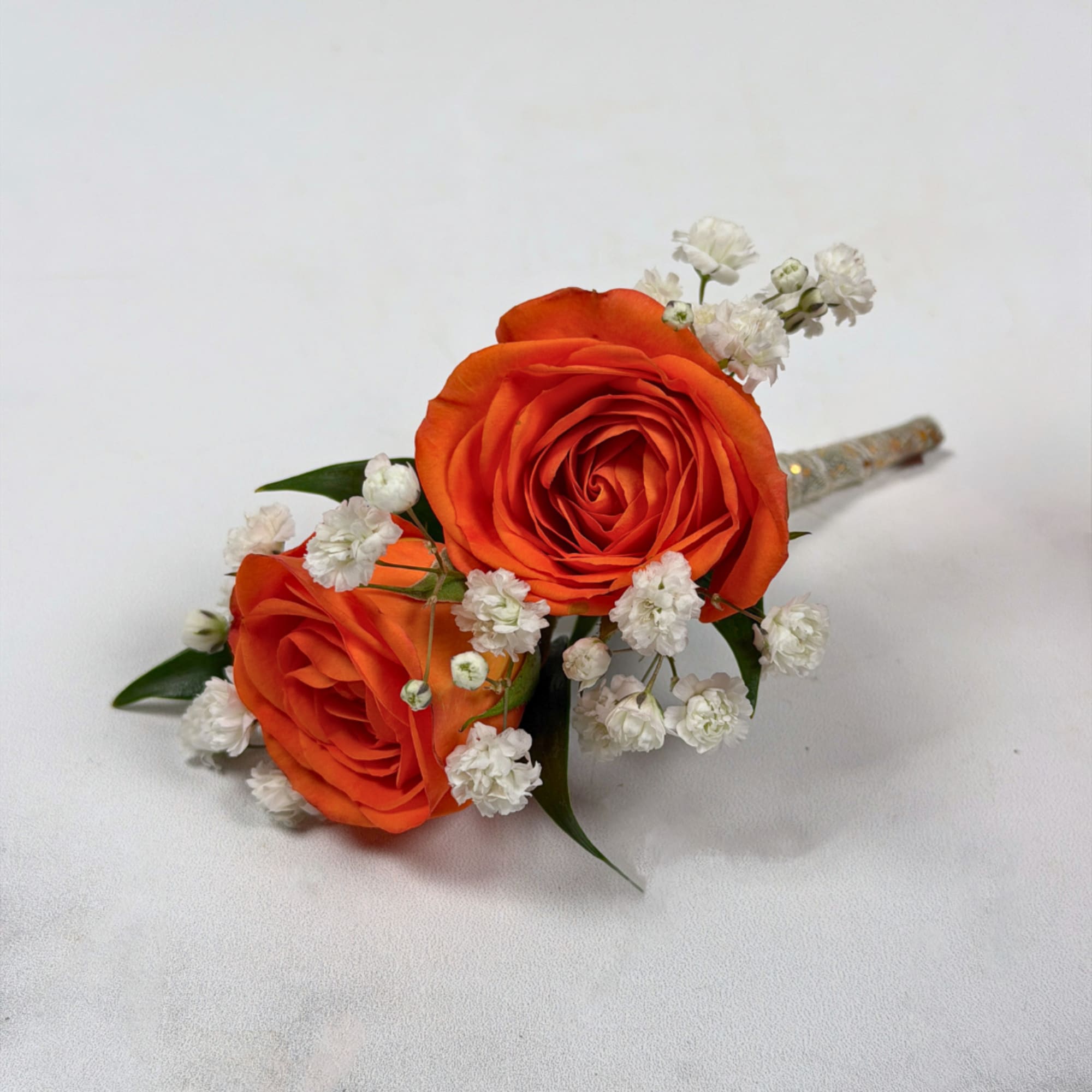 Two vivid orange rose blooms make this boutonniere a bright, celebratory accent