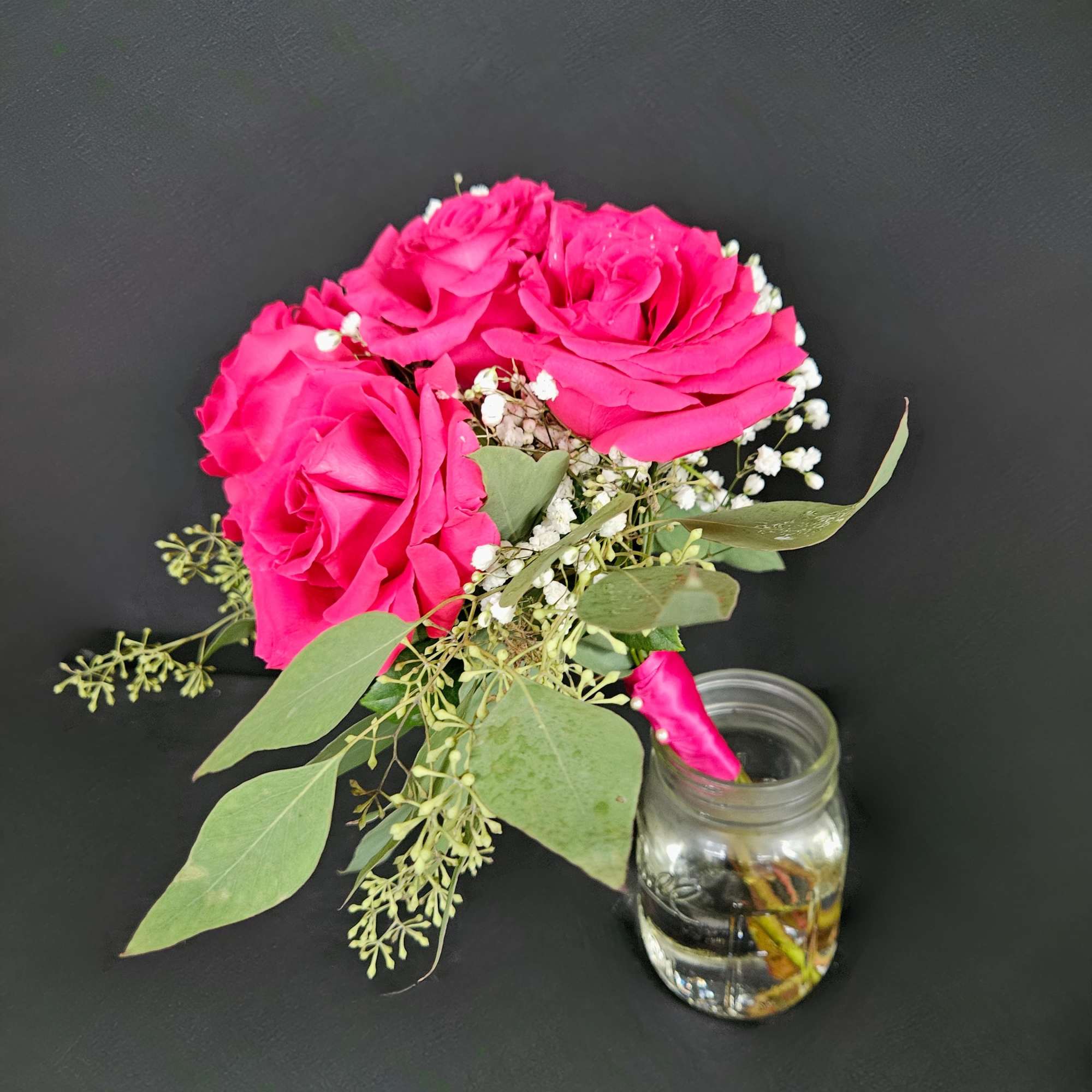 Pink roses with baby's breath and greenery beside a small glass jar