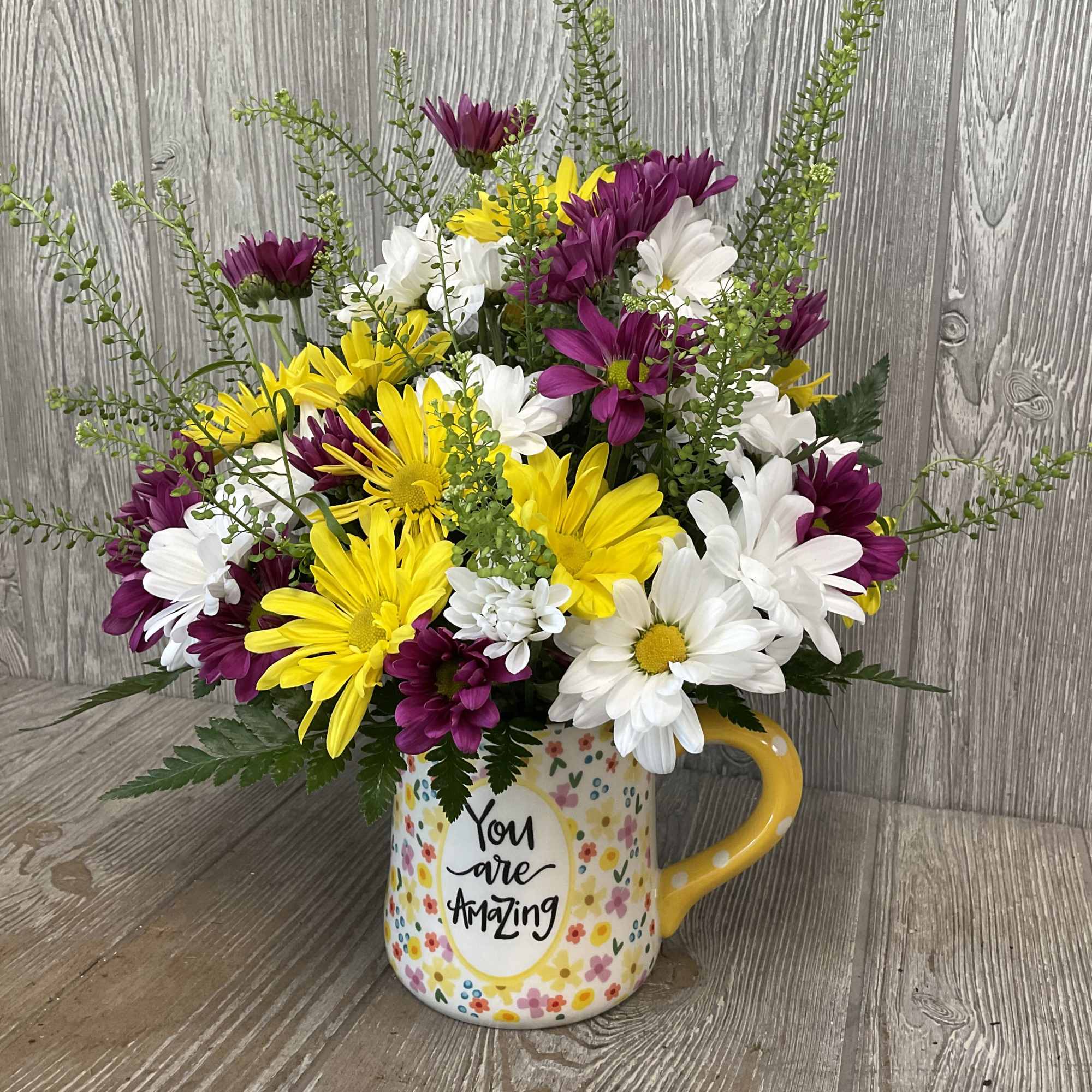 Bouquet of yellow, white, and purple daisies in a floral mug
