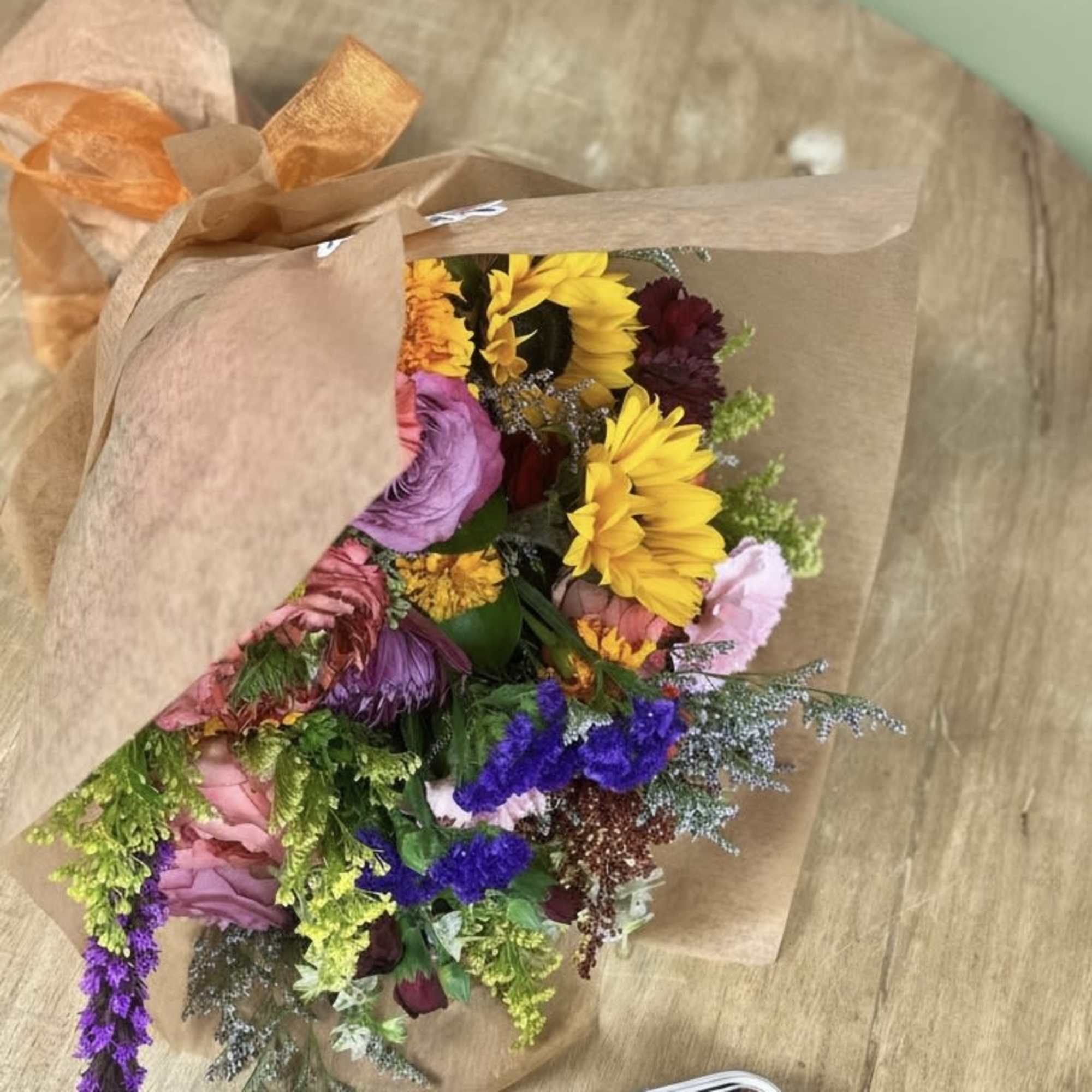 Colorful wrapped bouquet with sunflowers and mixed blooms beside a clear box of assorted macarons.