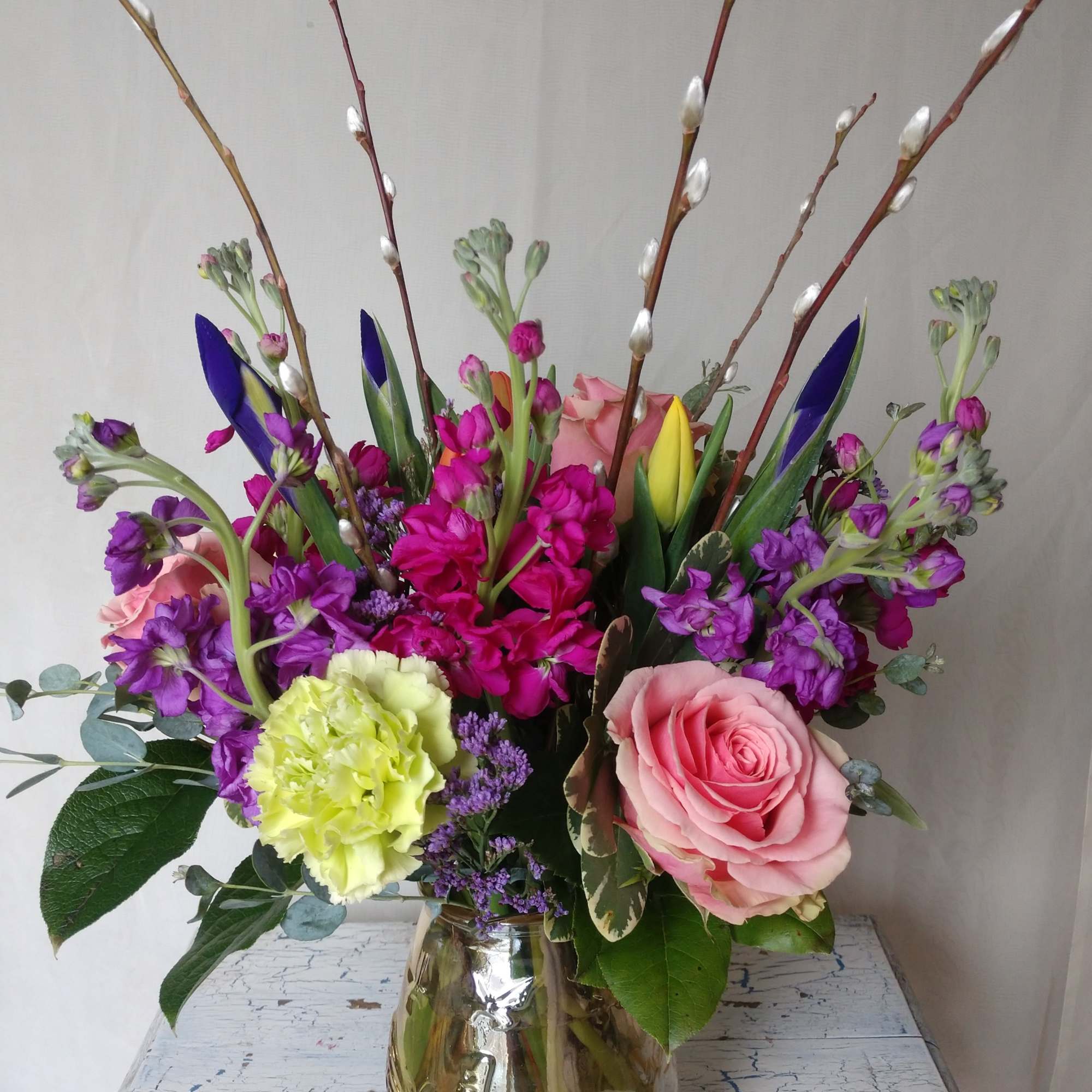 Mixed bouquet of pink roses, purple blooms, and pussy willow in a glass vase