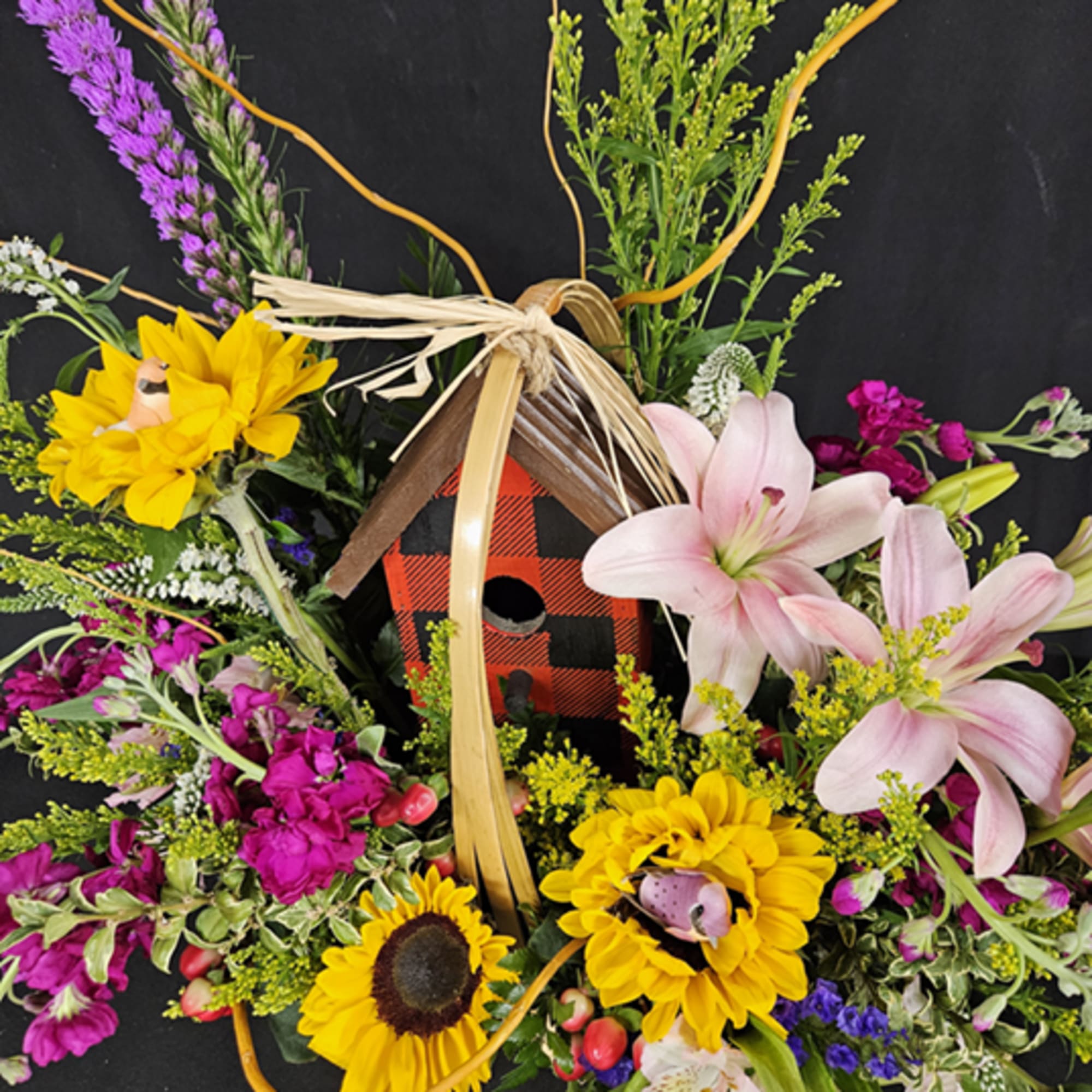 Colorful floral arrangement with sunflowers, pink lilies, and a birdhouse centerpiece