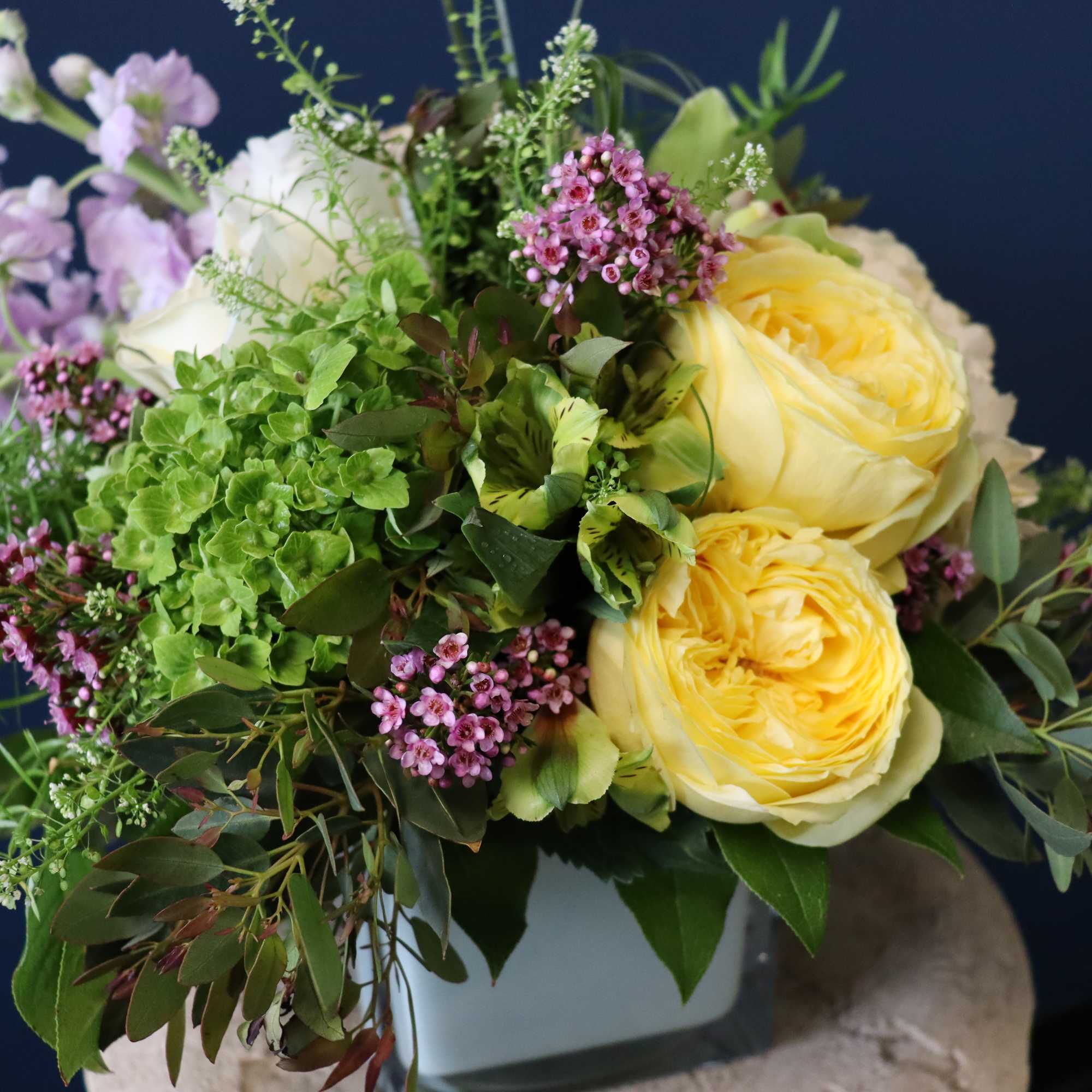 Bouquet of yellow roses, purple flowers, and greenery in a vase