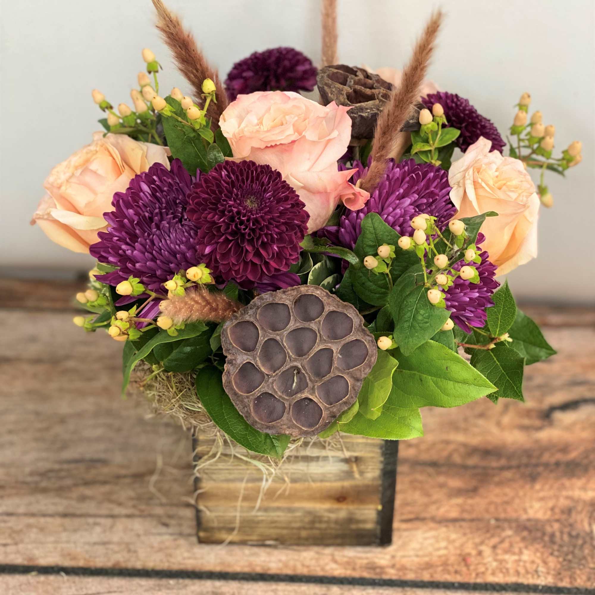 Purple and peach floral arrangement in a wooden box with dried accents