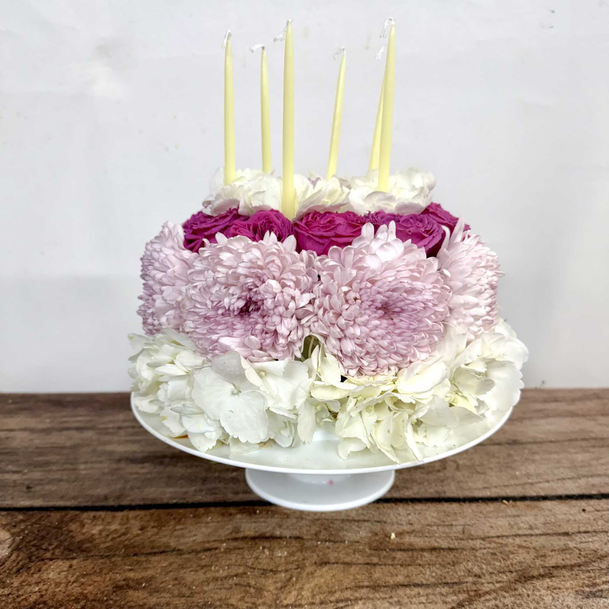 Round floral cake with pink, white, and cream blooms and tall candles