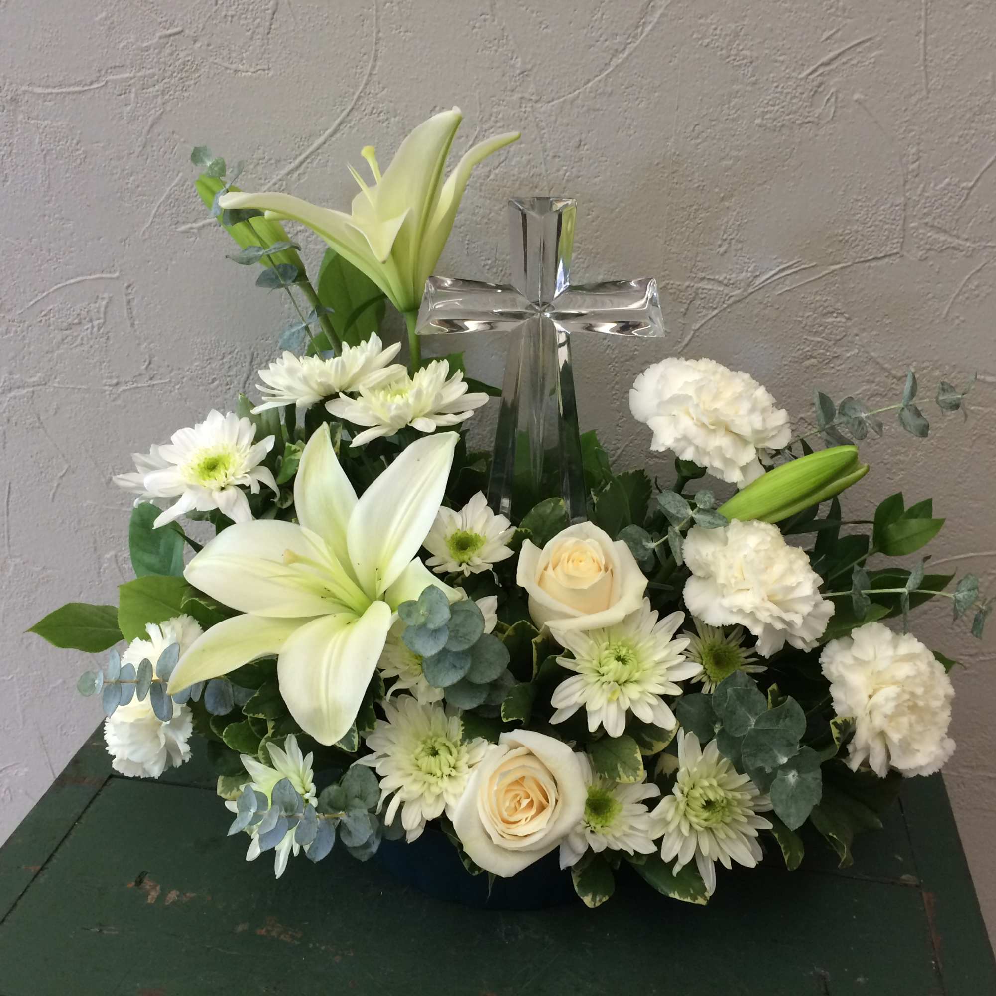 White floral arrangement with lilies, roses, and a clear glass cross