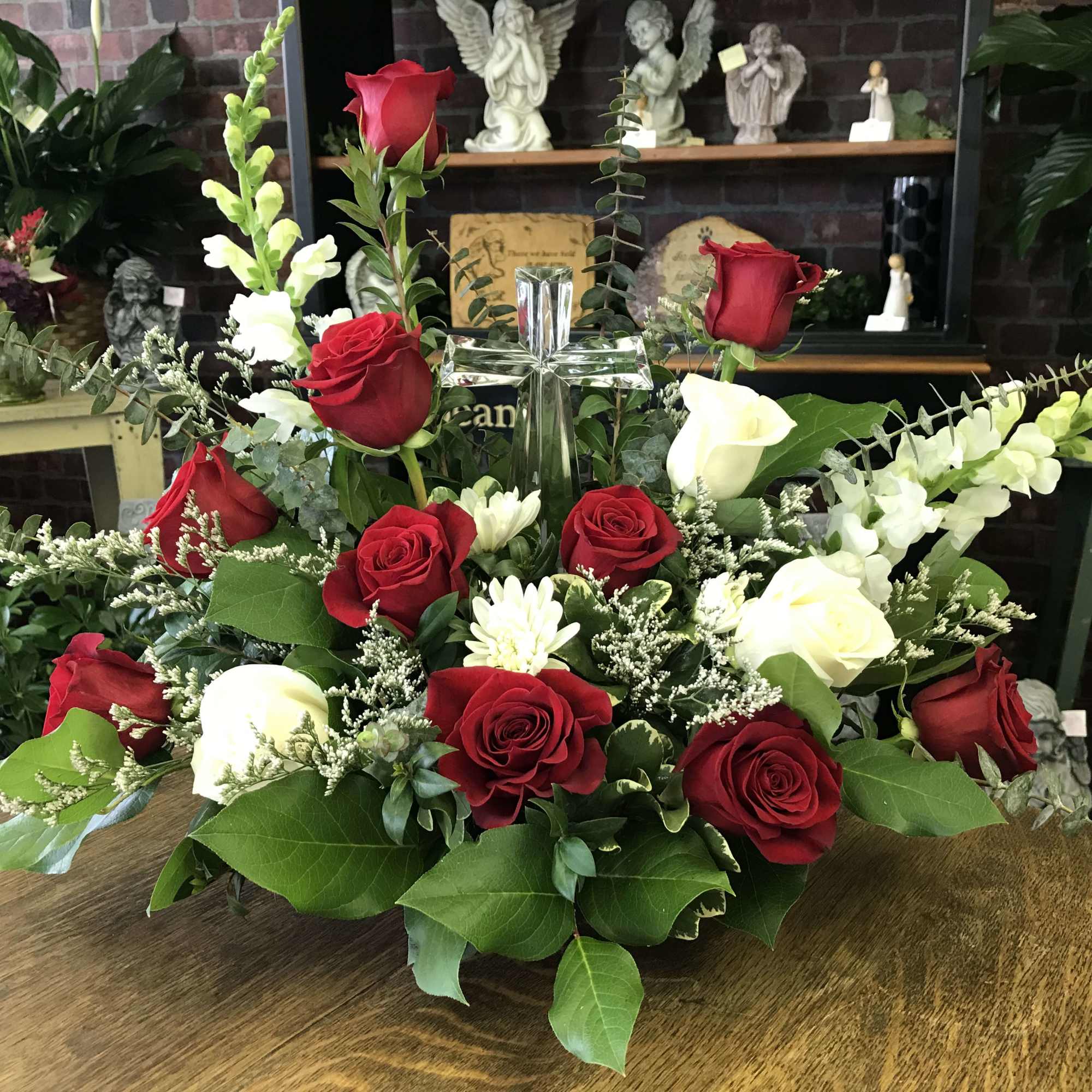 Red and white roses arranged around a clear glass cross