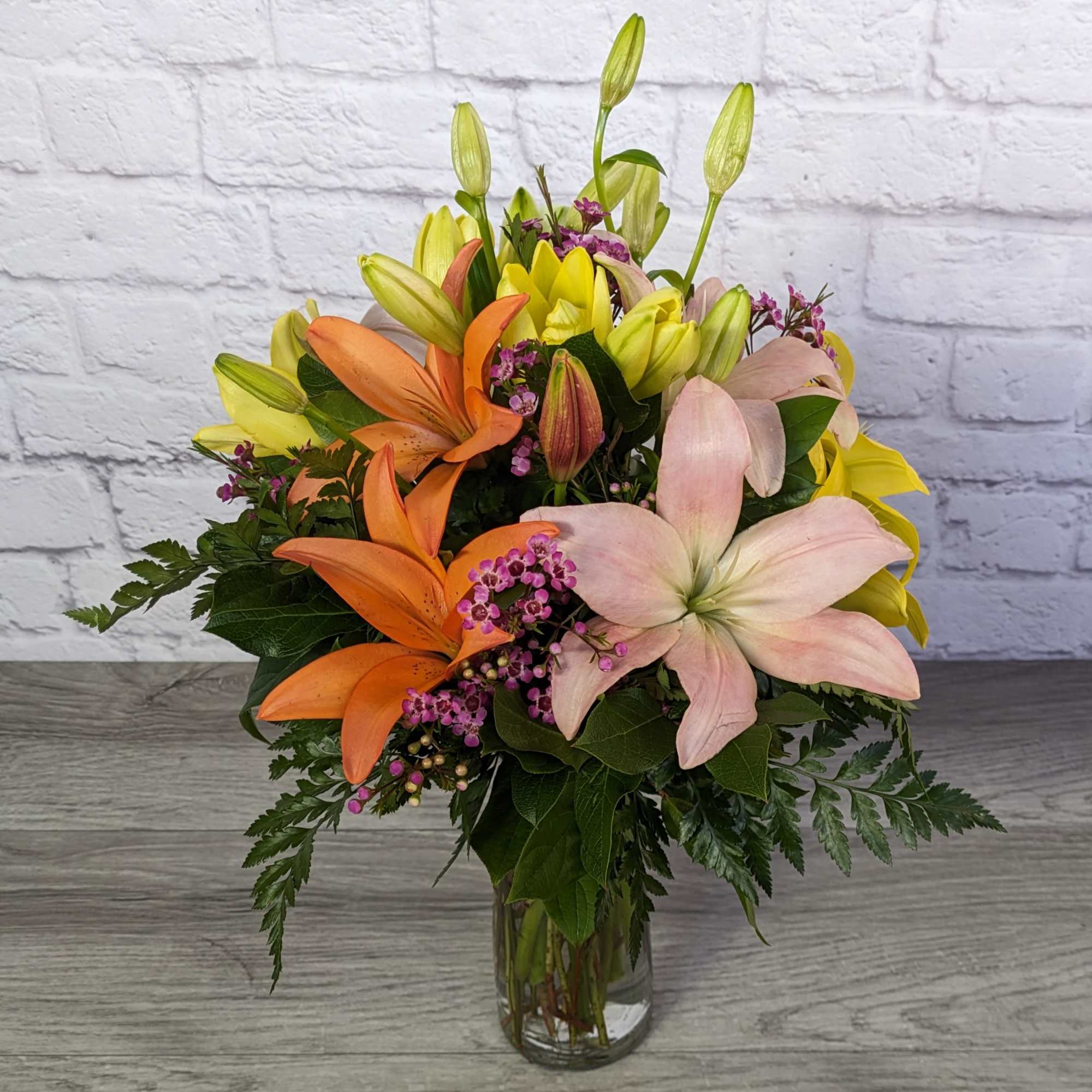 Bouquet of lilies in orange, pink, and yellow in a glass vase