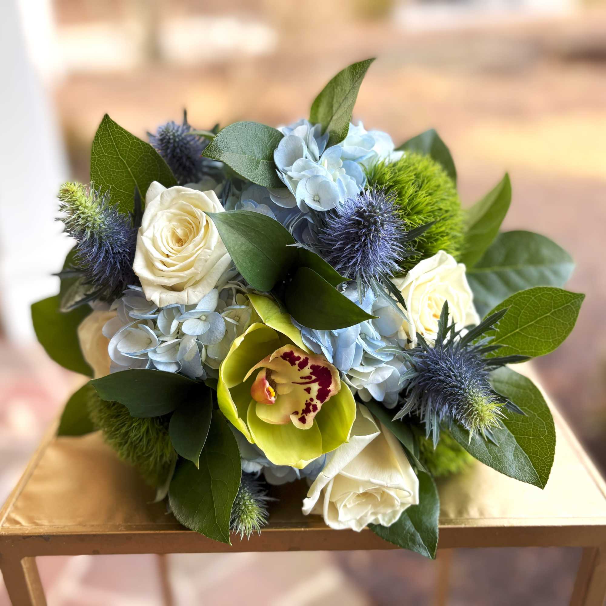 Compact bouquet of white roses, blue hydrangeas, green cymbidium orchid and blue thistle blooms