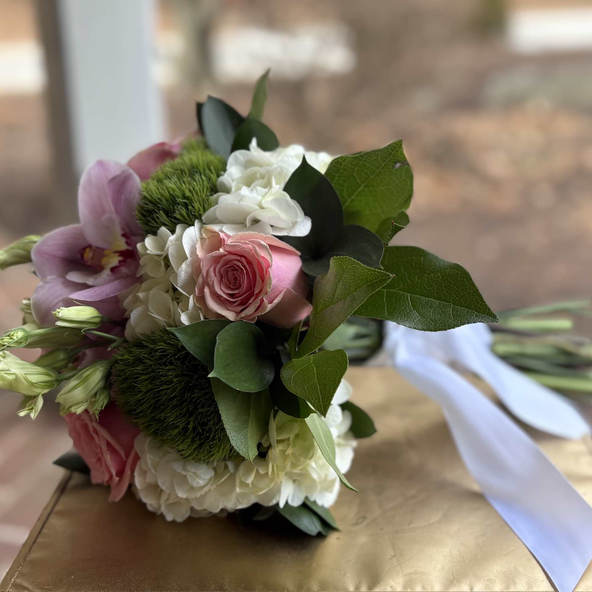 Hand-tied bouquet of pink roses, orchids, white hydrangea, and green blooms with a white ribbon.