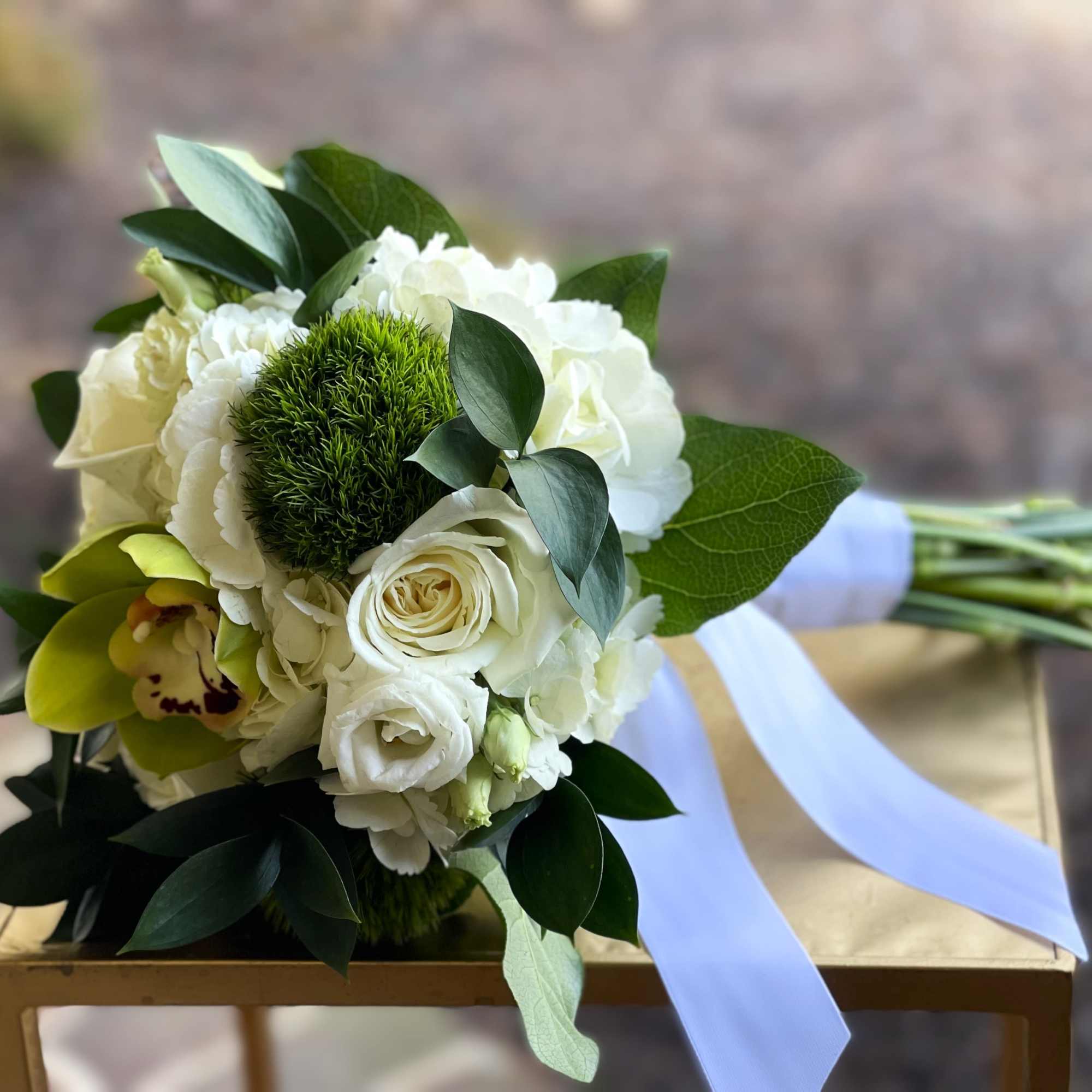 Hand-tied bouquet of white roses and hydrangeas with green accent blooms and orchid, tied with white ribbon.